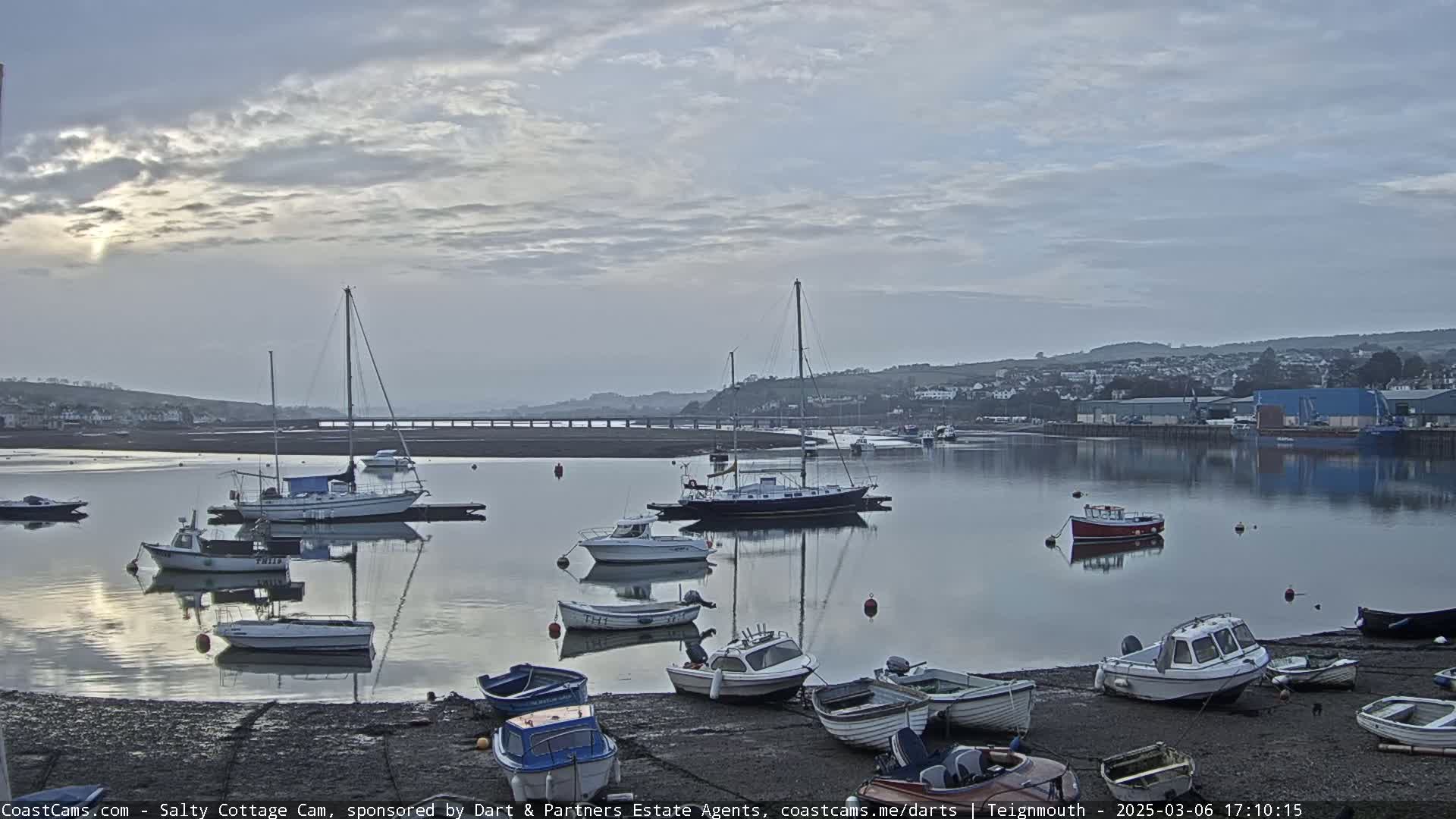 Many small boats and sailboats are moored in a calm harbor under a cloudy sky.