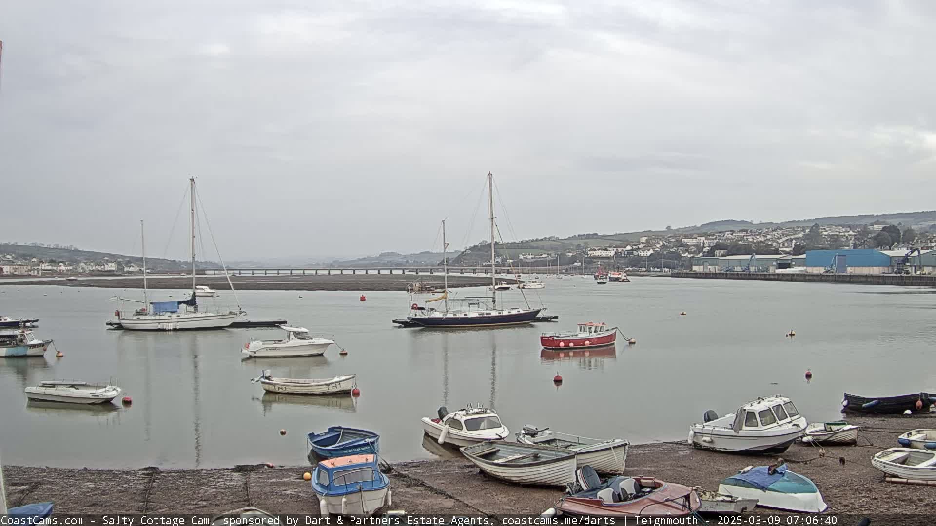 Several sailboats and motorboats are moored in a calm harbor under an overcast sky.