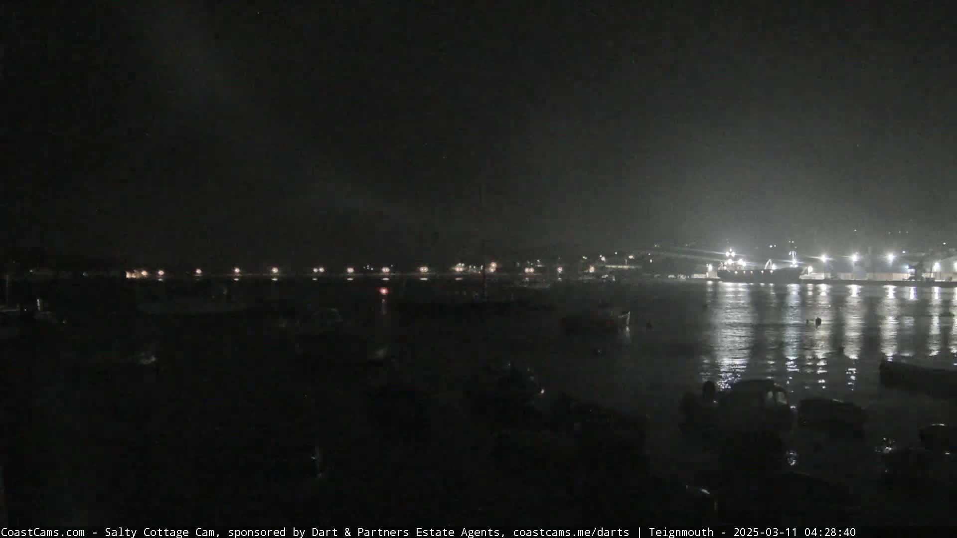 A nighttime view of a harbor with boats and lights reflecting on calm water.