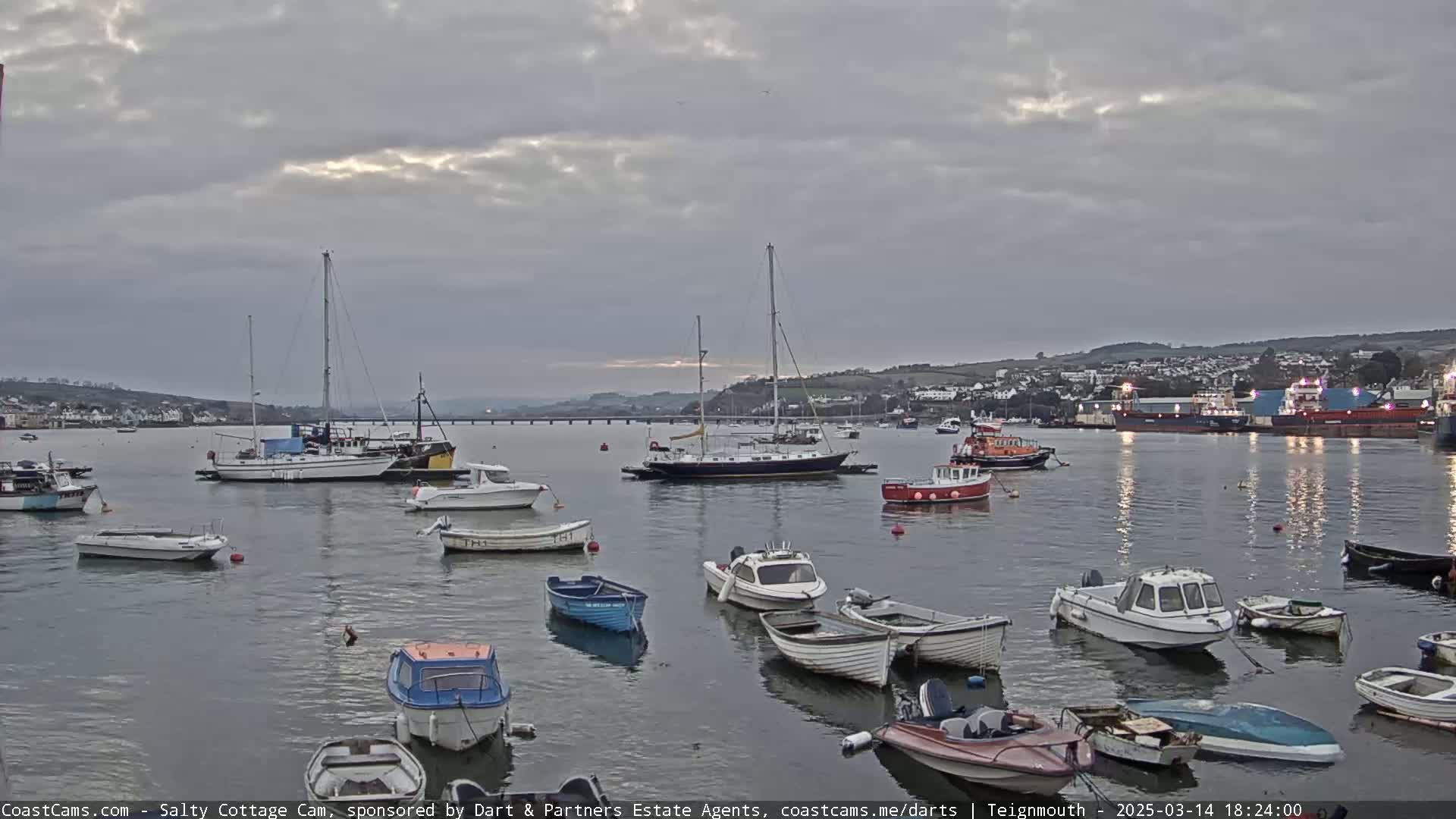 Many small motorboats and sailboats are moored in a calm harbor under an overcast sky.