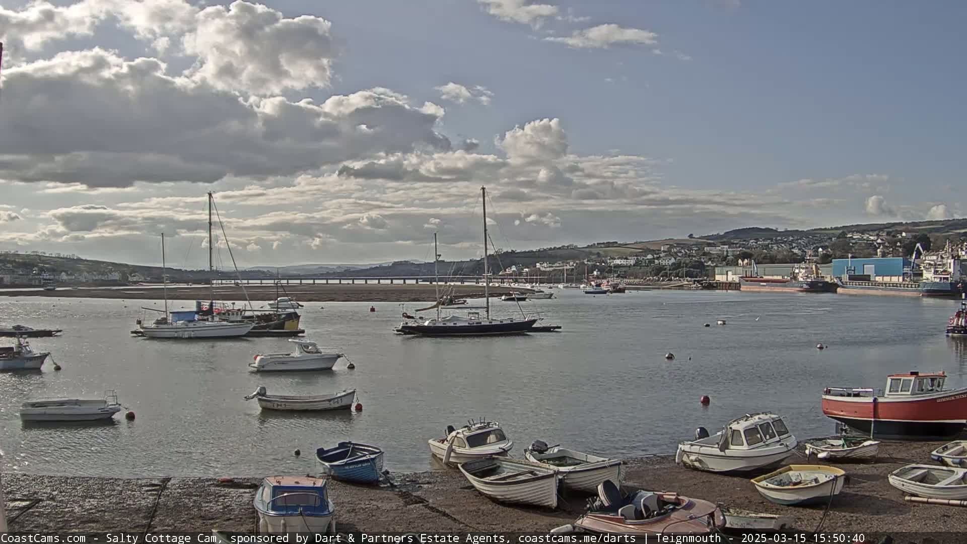 A calm harbor scene with numerous sailboats and motorboats, under a partly cloudy sky.