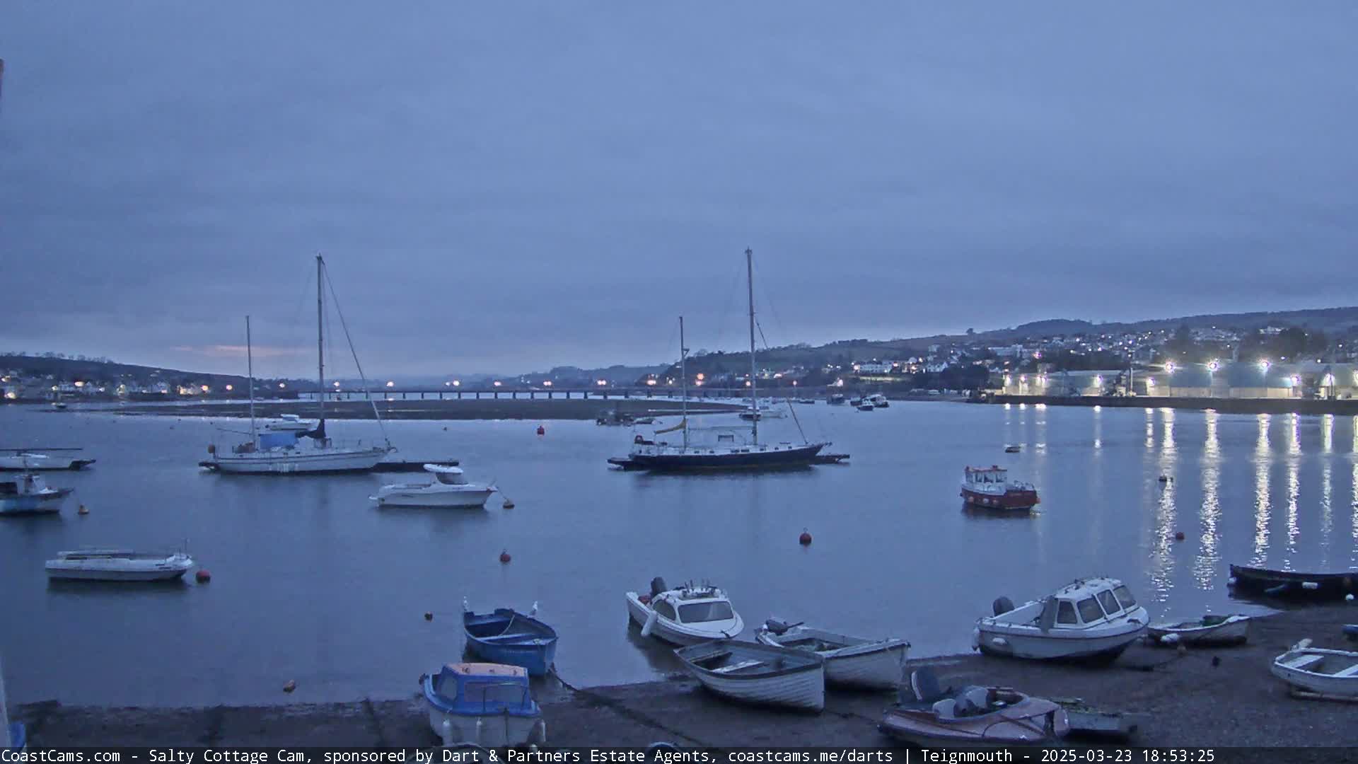Numerous boats are moored in a calm harbor at twilight under a dusky sky.