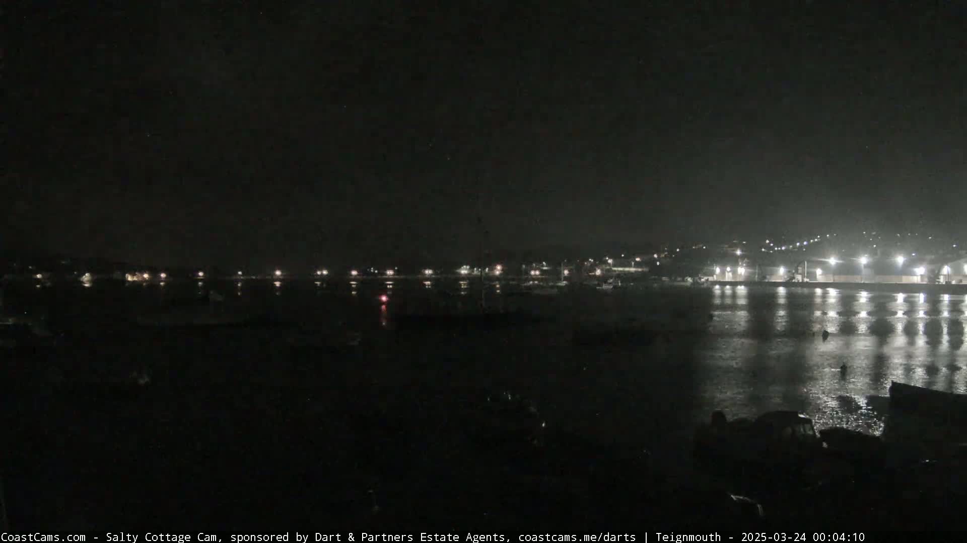 A nighttime view of a calm body of water with a town's lights reflecting on its surface.