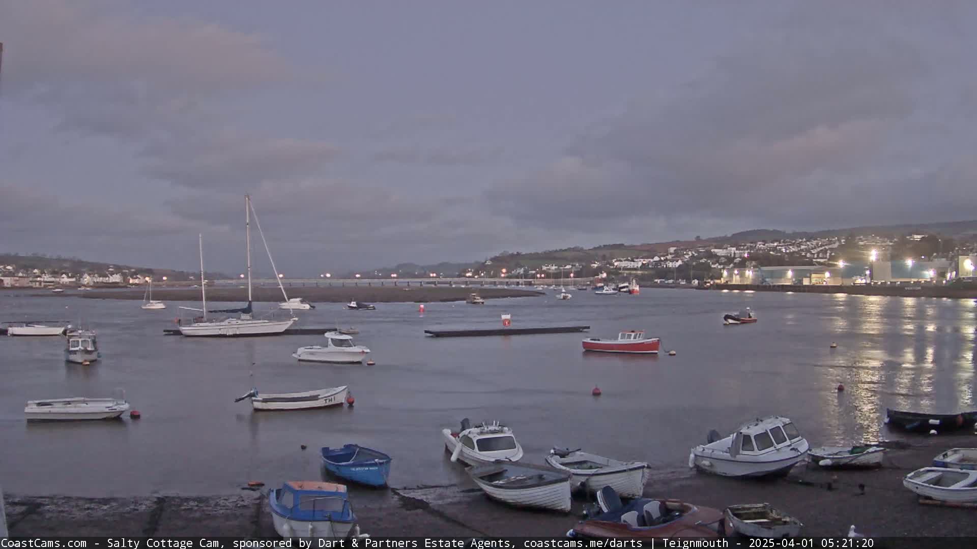 Numerous small boats and sailboats are moored in a calm harbor at dusk under a cloudy sky.