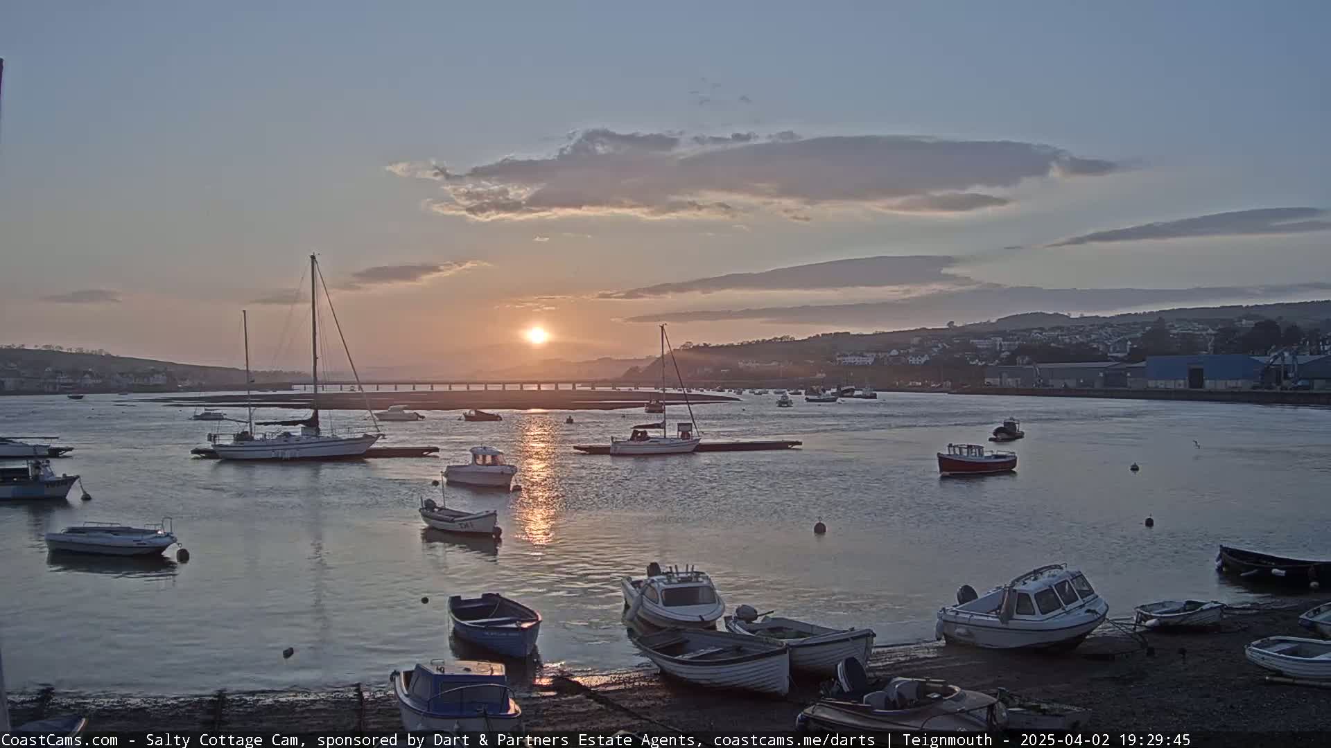 Numerous small boats are moored in a calm harbor at sunset under a partly cloudy sky.