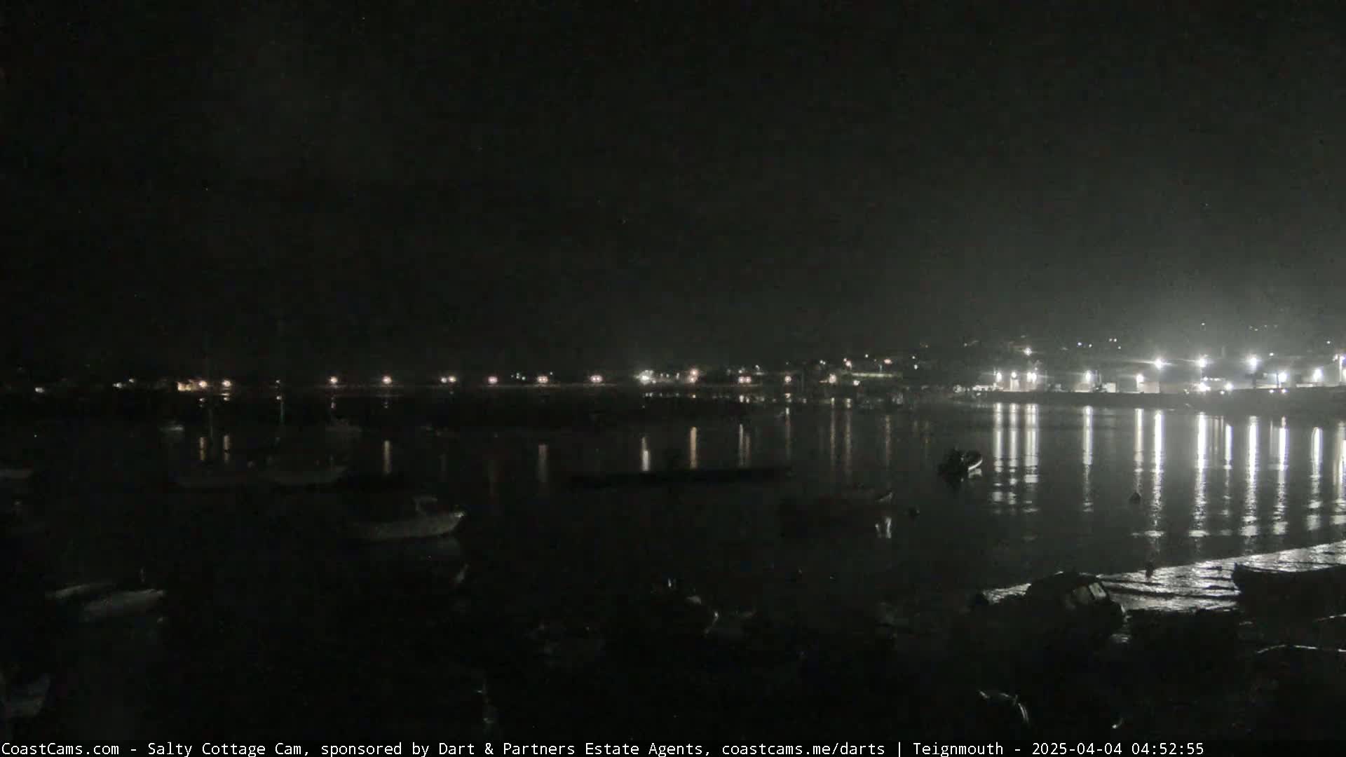 A nighttime view of a harbor with boats and lights reflecting on calm water.