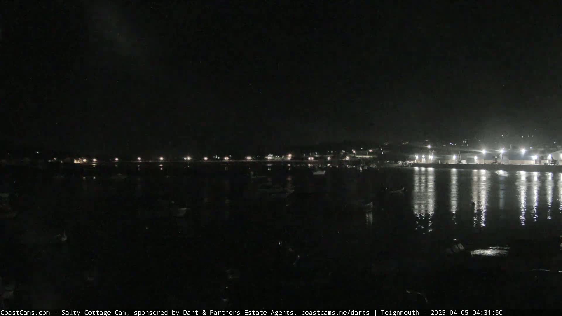 A nighttime view of a harbor with numerous boats and lights reflecting on the calm water.