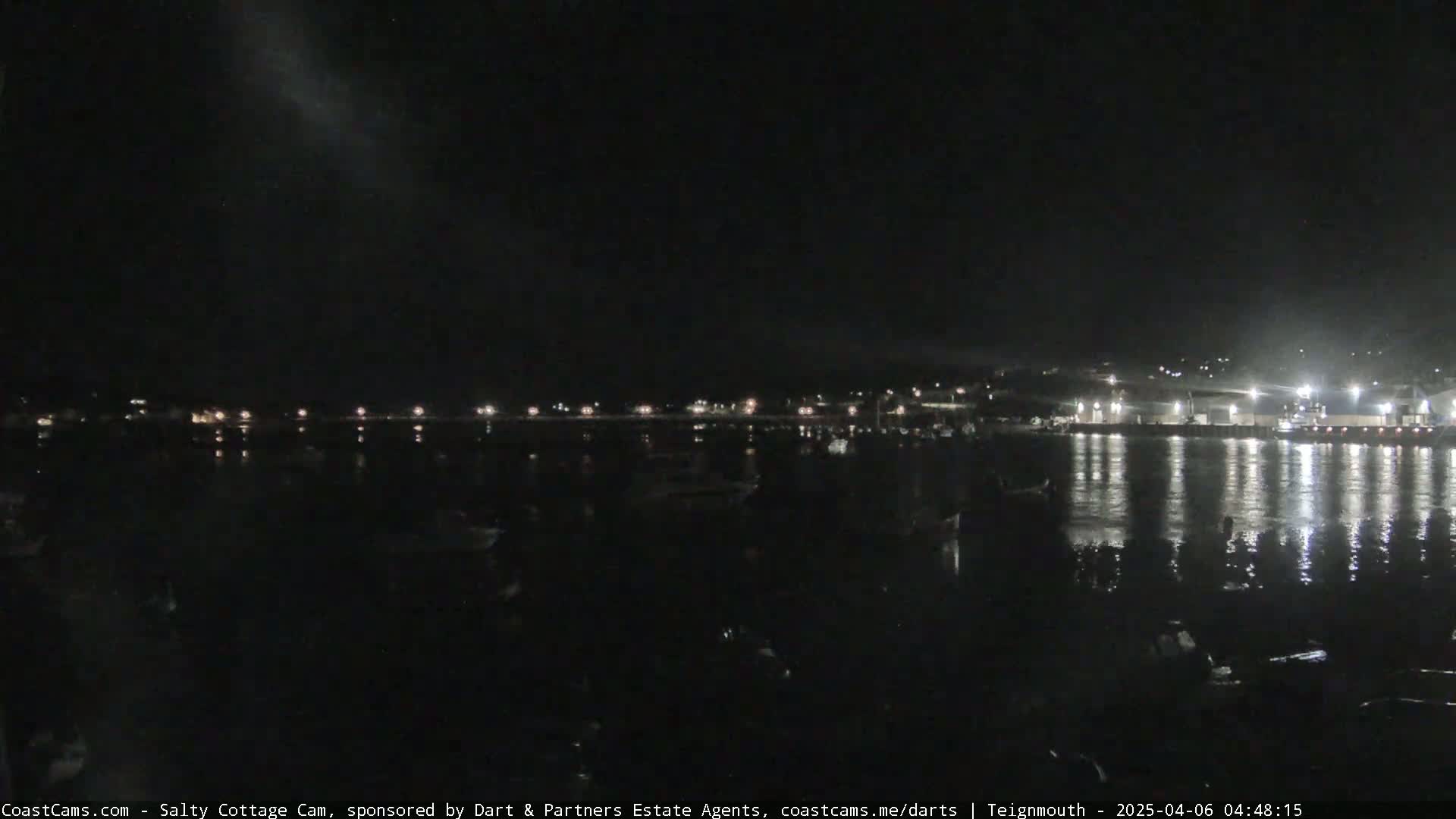 A nighttime view of a harbor, with lights reflecting on calm water and a dark sky.
