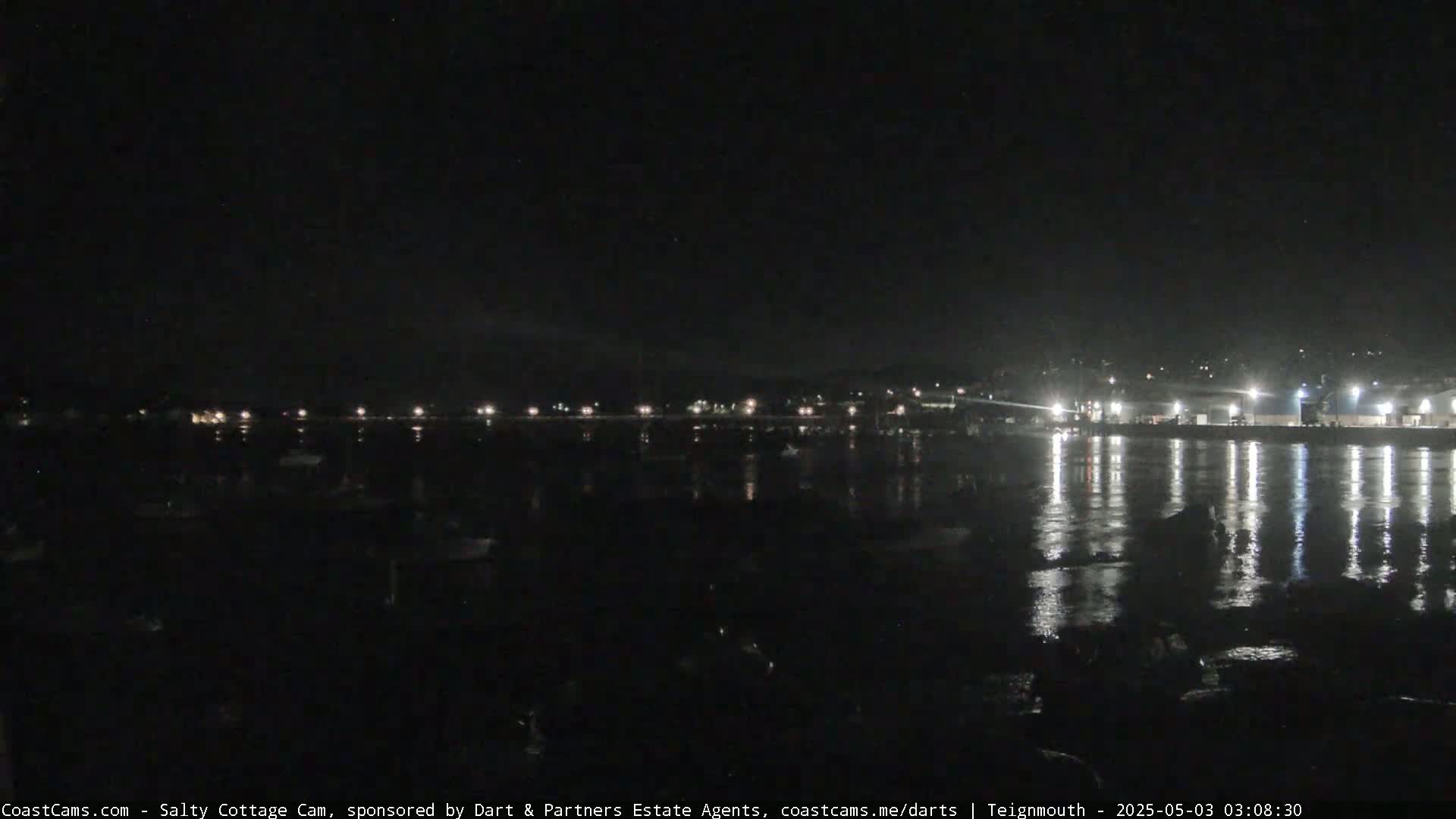A nighttime view of a harbor with boats and lights reflecting on calm water.