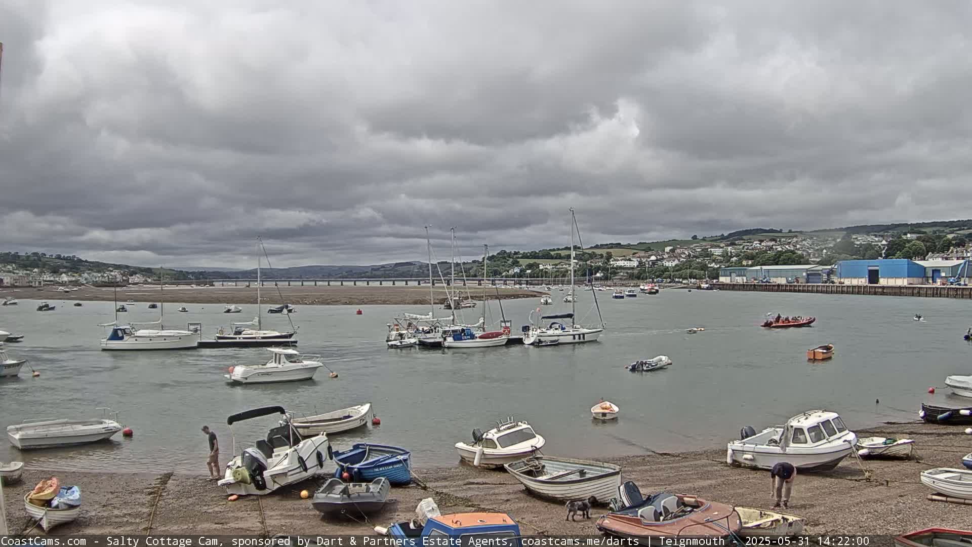 Many boats are moored in a calm harbor under a cloudy sky.