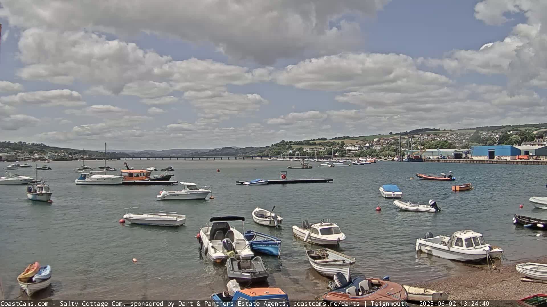 A partly cloudy day shows many small motorboats moored in a harbor with a bridge in the distance.