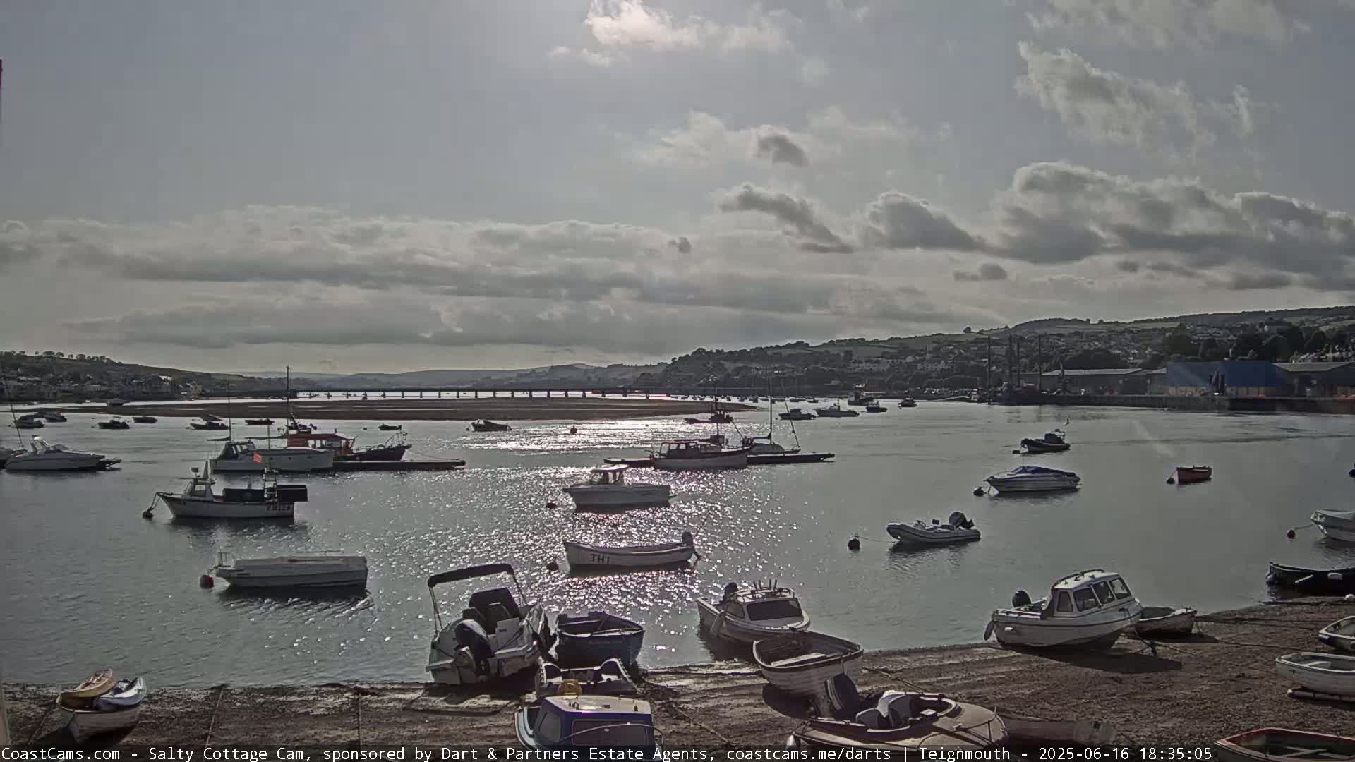 Numerous small boats are moored in a calm harbor under a partly cloudy sky.