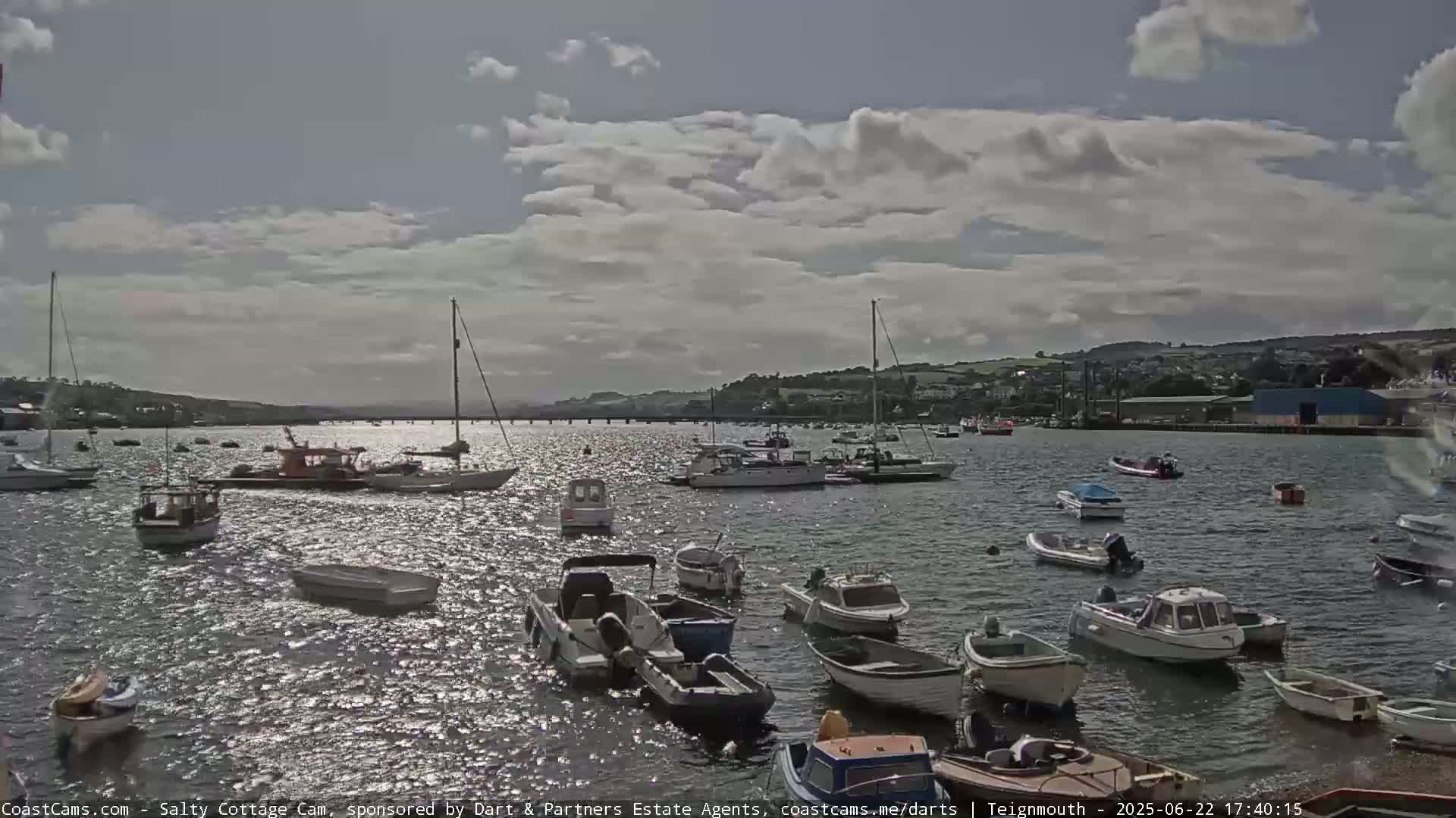 Numerous small boats are moored in a calm harbor under a partly cloudy sky.