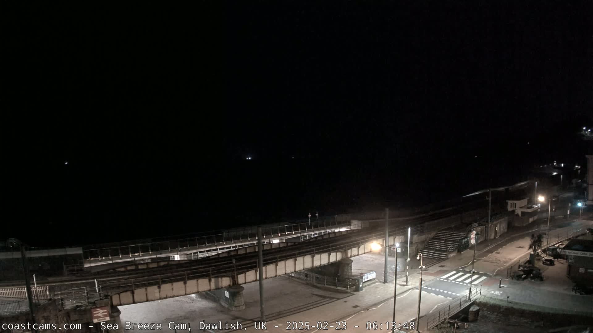 A nighttime view of a coastal railway line and road crossing under a dark sky.