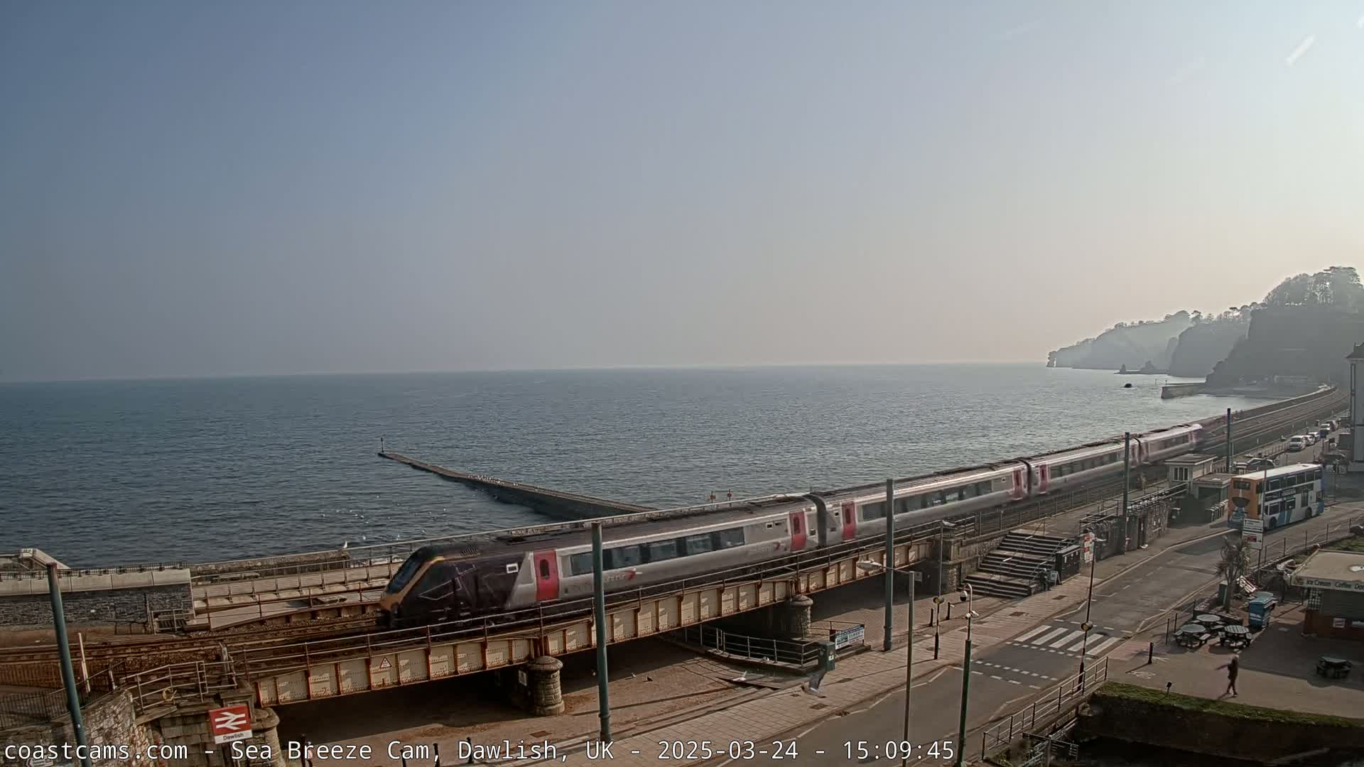 A train crosses a bridge by the sea on a clear, sunny day.