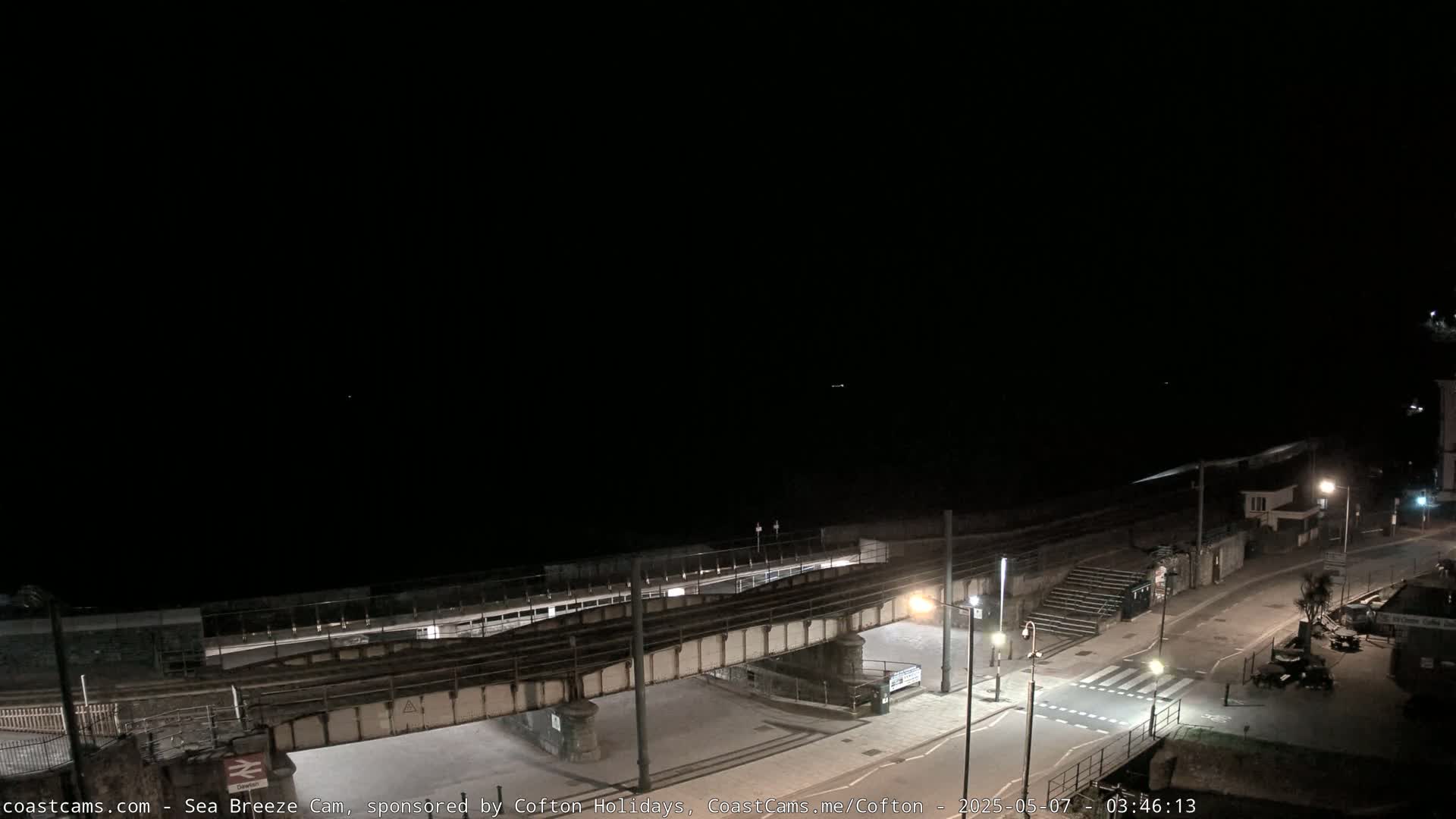 A dark nighttime scene shows a coastal road, a railway bridge, and a mostly dark ocean.