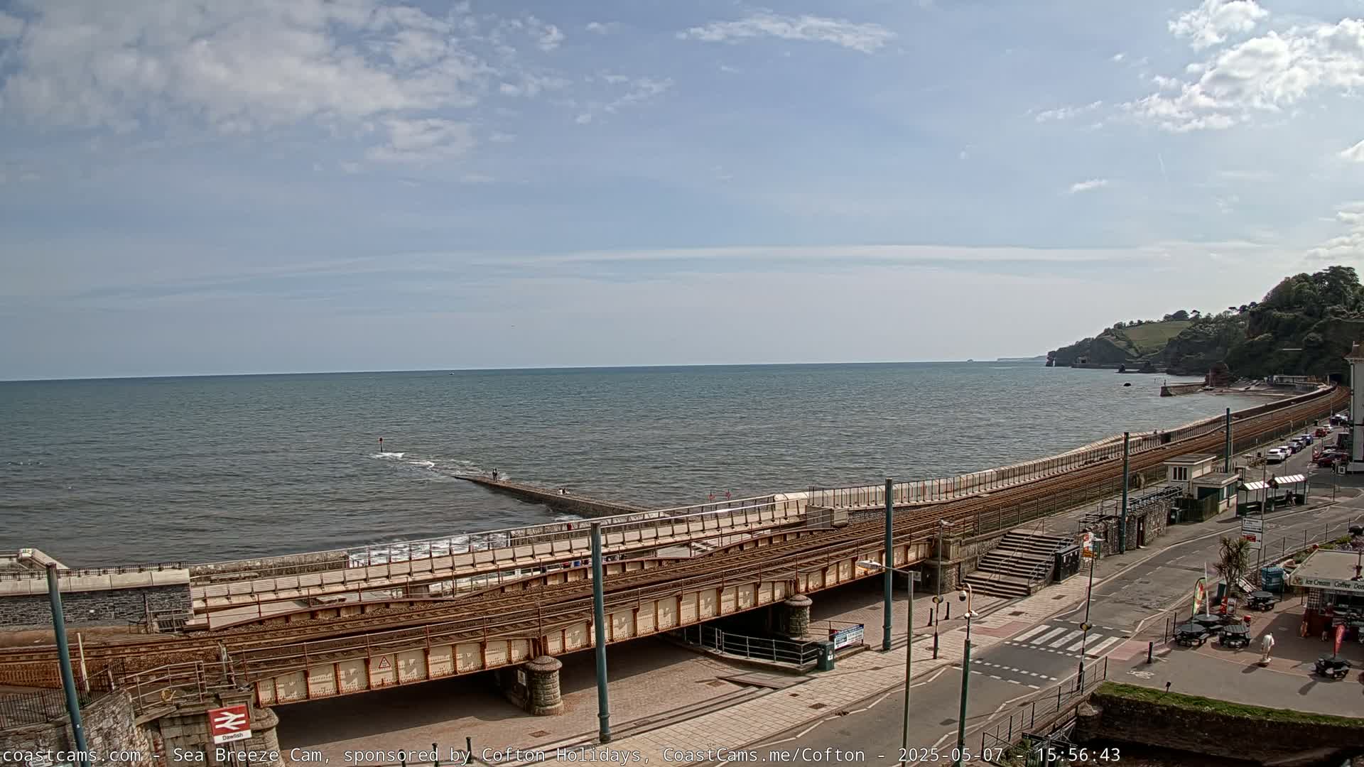 A seaside town with a train track running along a sea wall under partly cloudy skies.