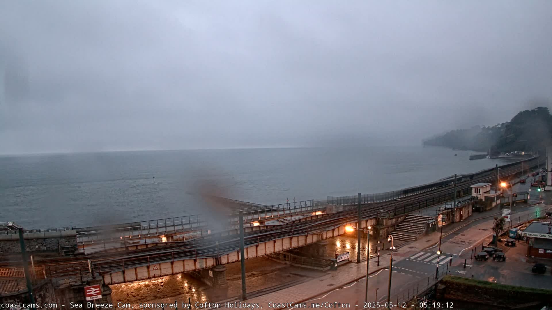 A misty overcast day reveals a coastal town with railway tracks crossing a bridge over a body of water.