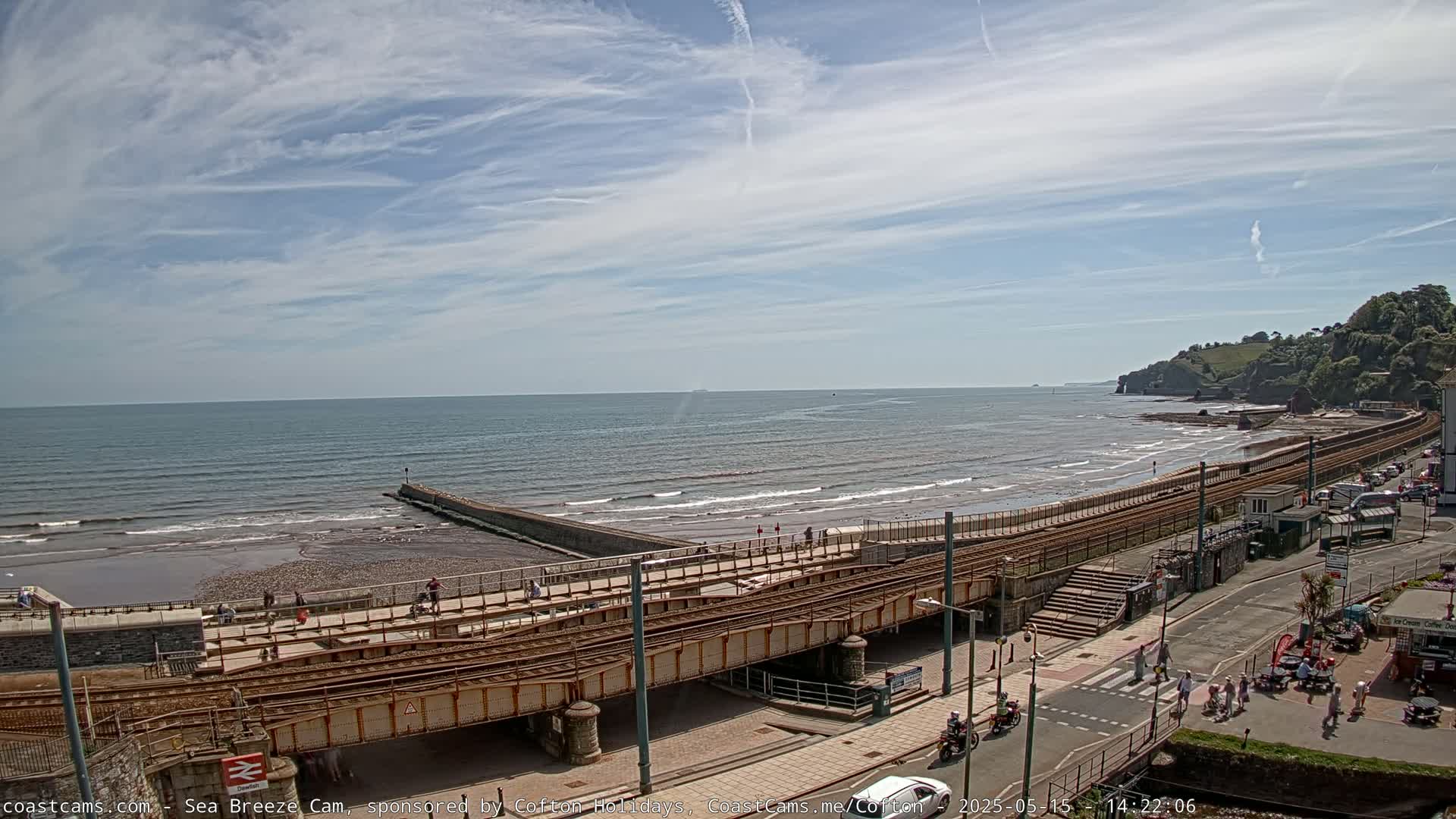 A beach with a railway line running alongside it, under a partly sunny sky with some clouds.