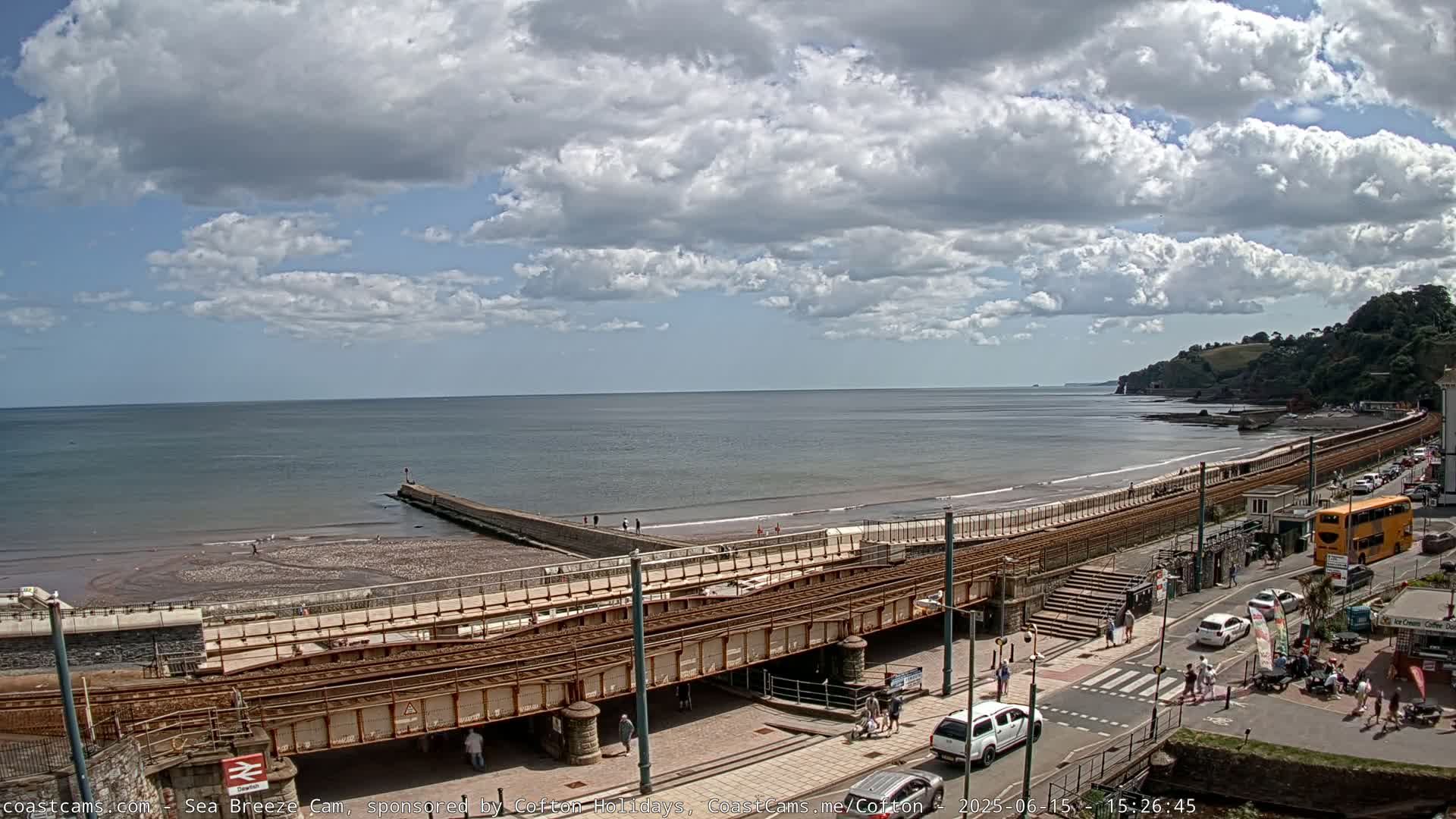 A seaside town with a train track running along the beach, under partly cloudy skies.