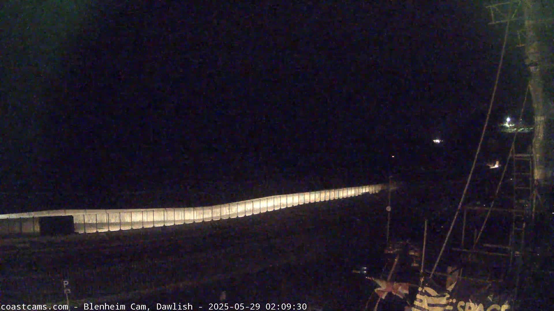 A long, illuminated barrier stretches across a dark, nighttime scene, with a portion of a structure visible in the bottom right corner.