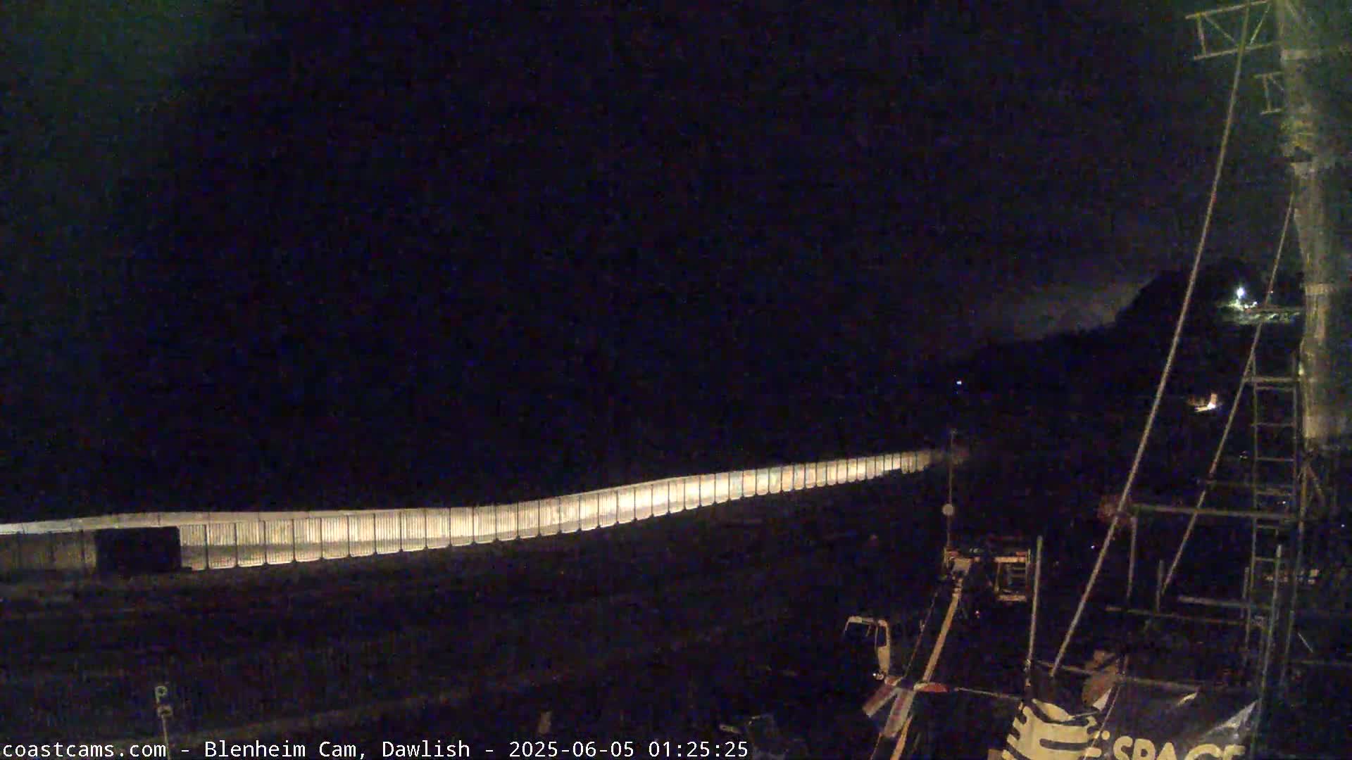 A long, illuminated barrier stretches across a dark, nighttime scene, with some machinery visible in the lower right corner.