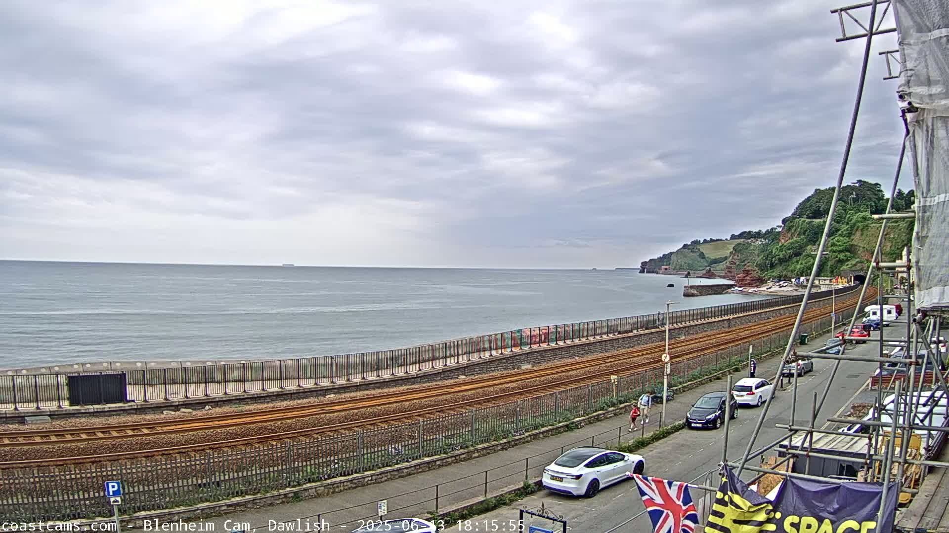 A coastal railway line runs alongside a sea wall, overlooking a calm sea under a cloudy sky.