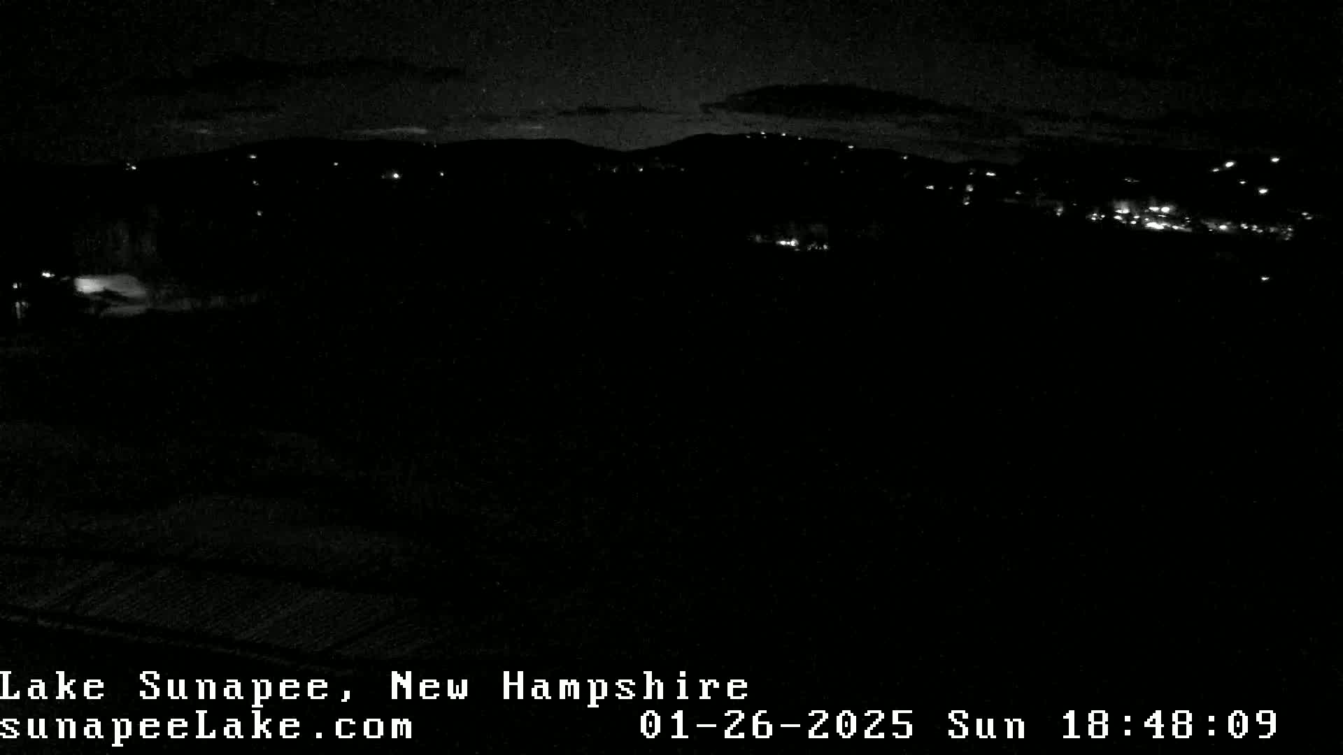 A nighttime, low-light view shows a dark landscape with sparsely scattered lights in the distance under a mostly clear sky.