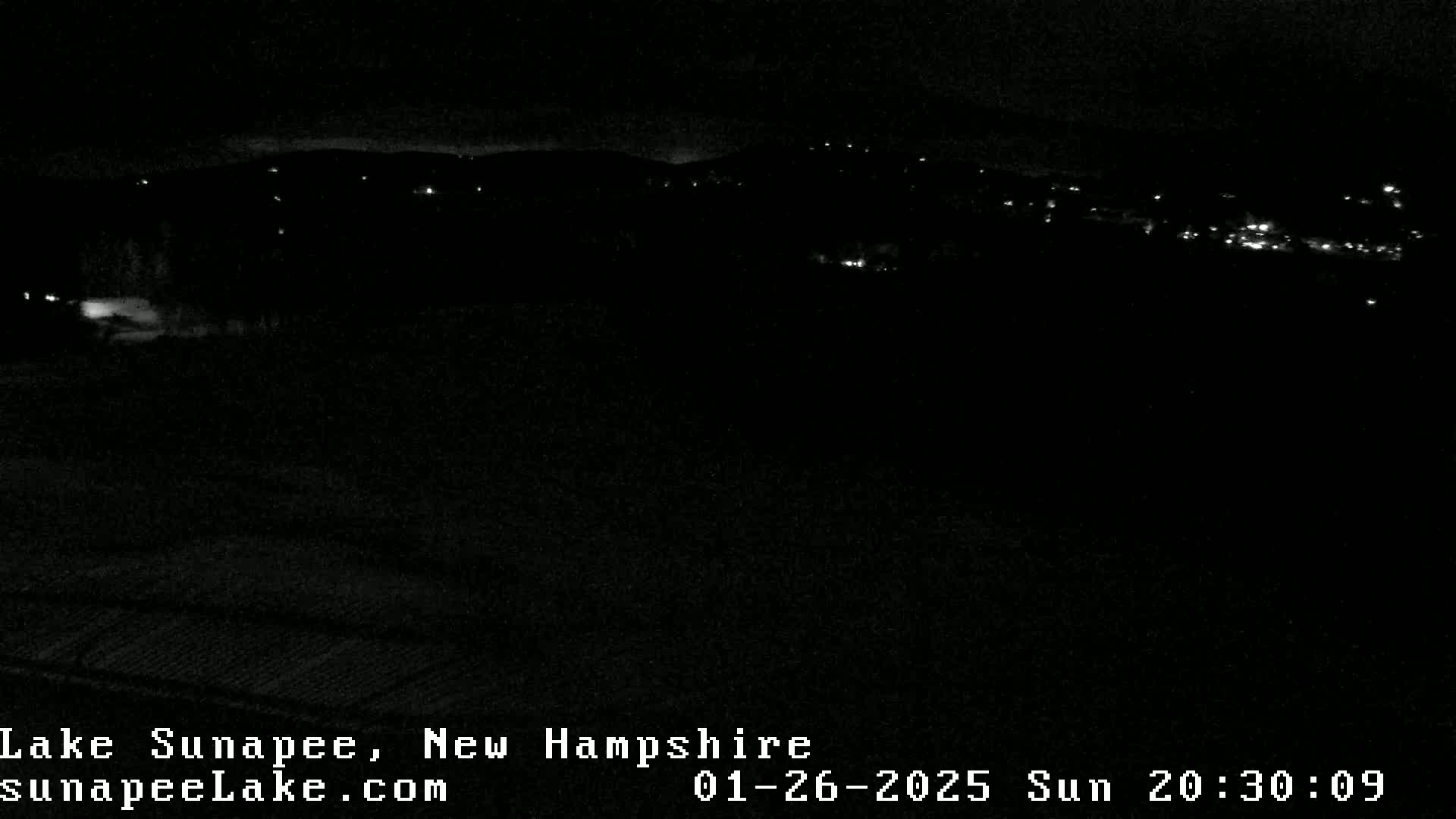 A nighttime, low-light view of a distant, dimly lit town nestled in a dark landscape.