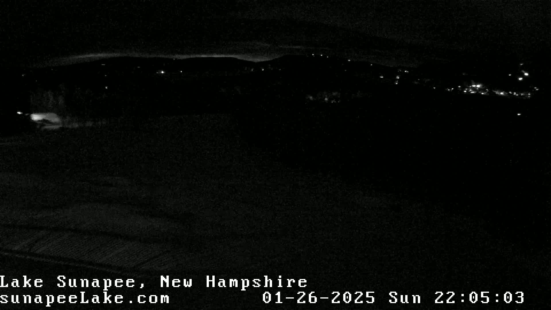 A nighttime long shot shows a dark landscape with a few distant lights under a mostly clear sky.