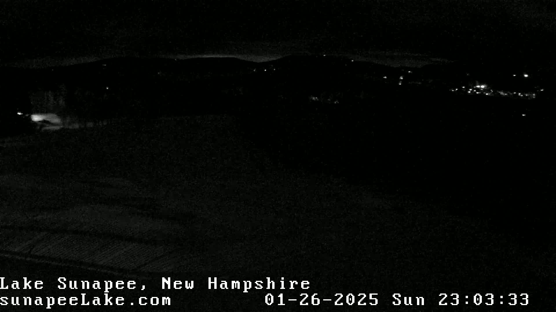 A nighttime, low-light view of a dark landscape with a few distant lights visible.