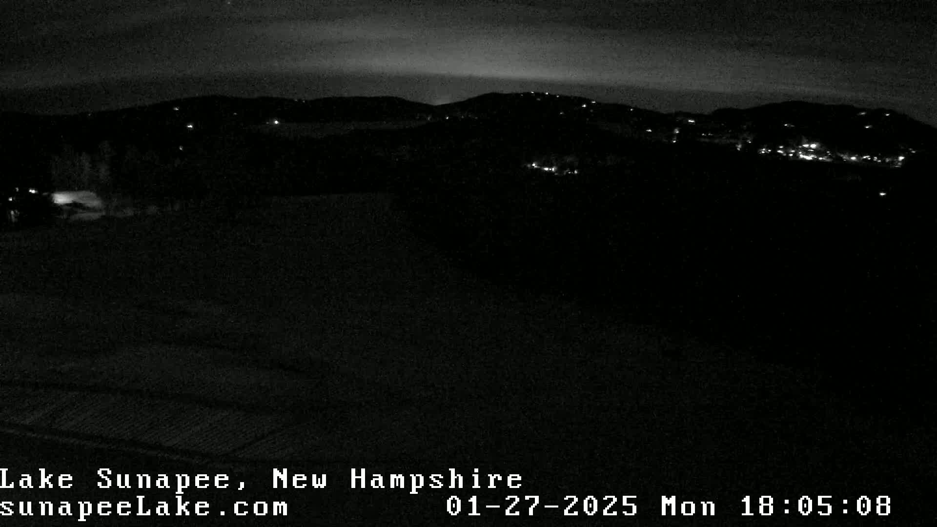 A nighttime, low-light view of dark hills with a few scattered lights visible in the distance.