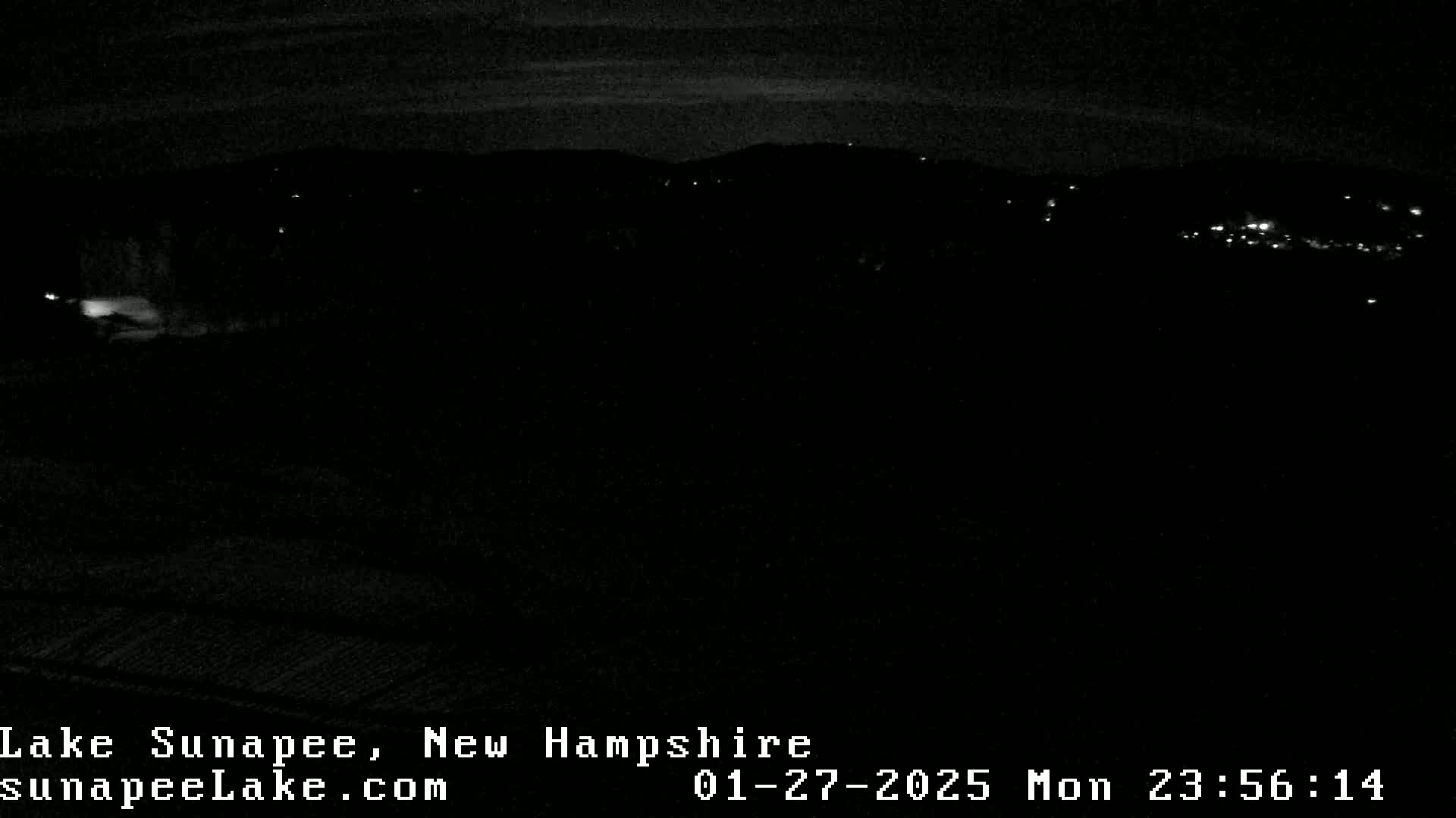 A nighttime, low-light view of a dark landscape with a few distant lights visible.