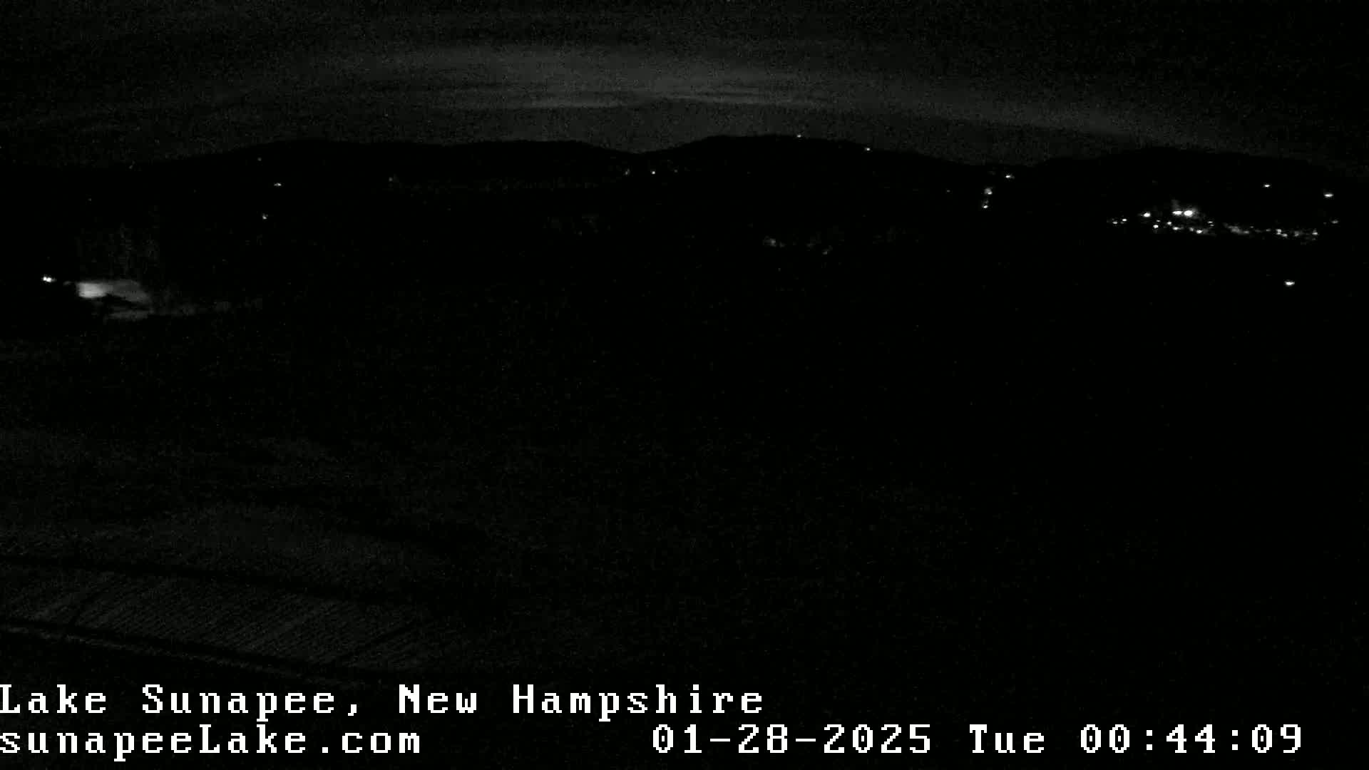 A nighttime, dark landscape shows a few distant lights against a mostly black sky.