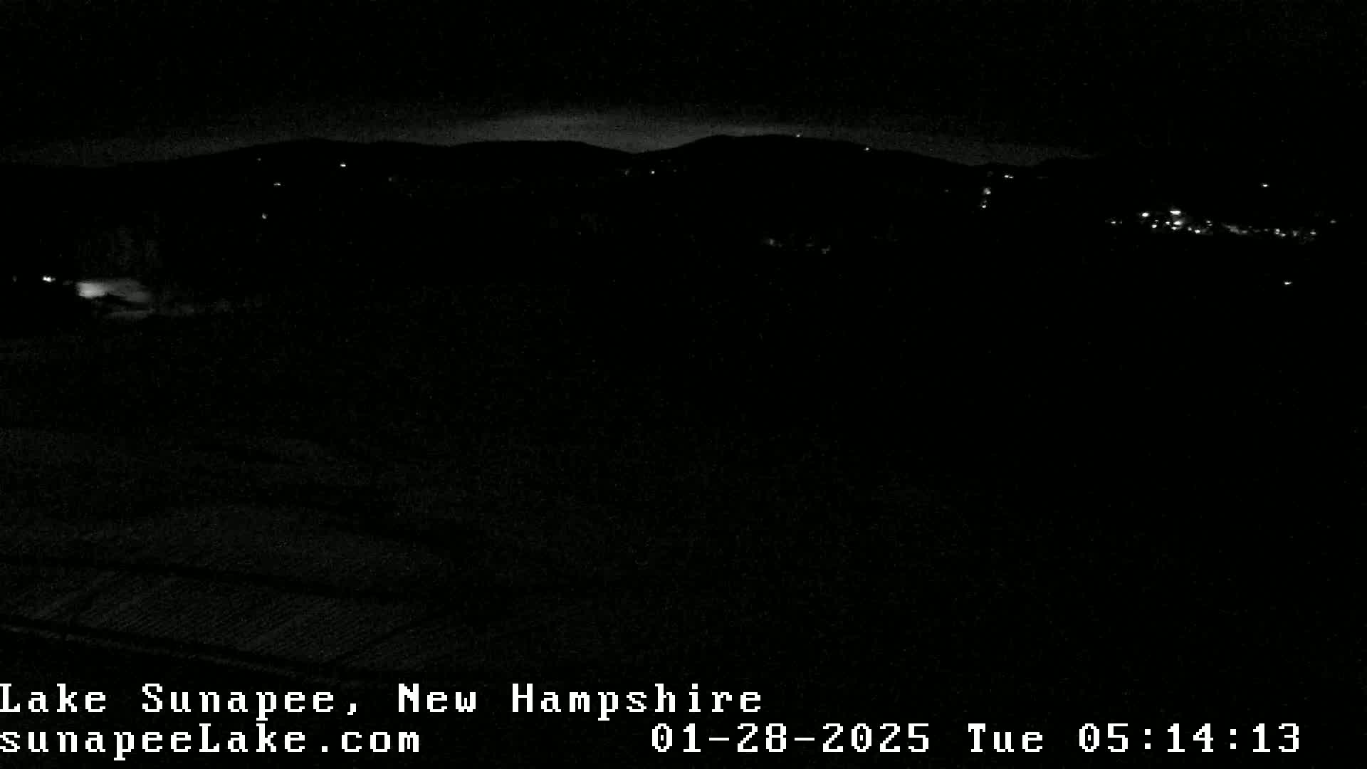 A nighttime view of a dark landscape with a few distant lights and a dark, possibly cloudy sky.