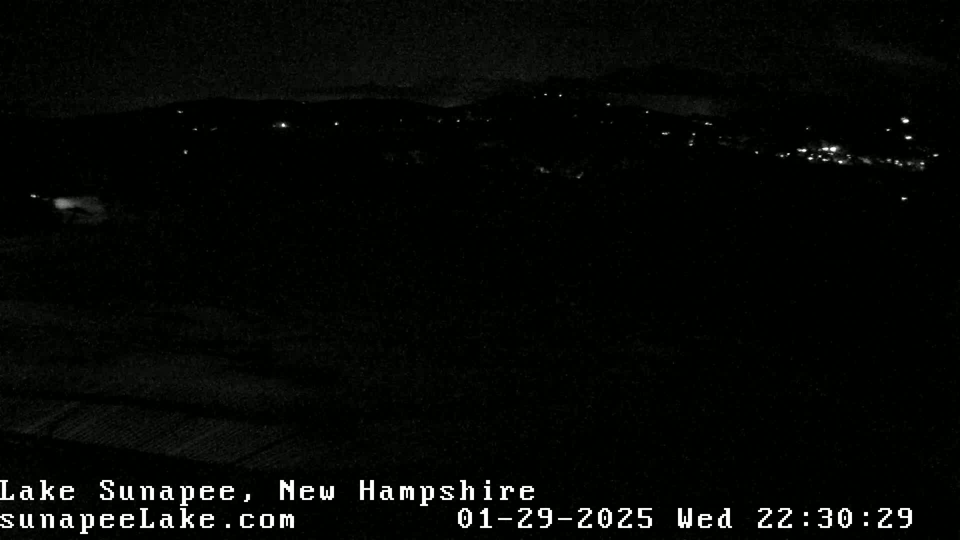 A nighttime, low-light view of a dark landscape with sparsely scattered lights in the distance.