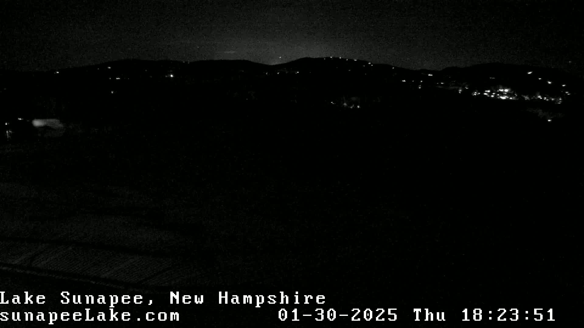 A nighttime, dark view of a distant hillside with scattered lights under a clear sky.