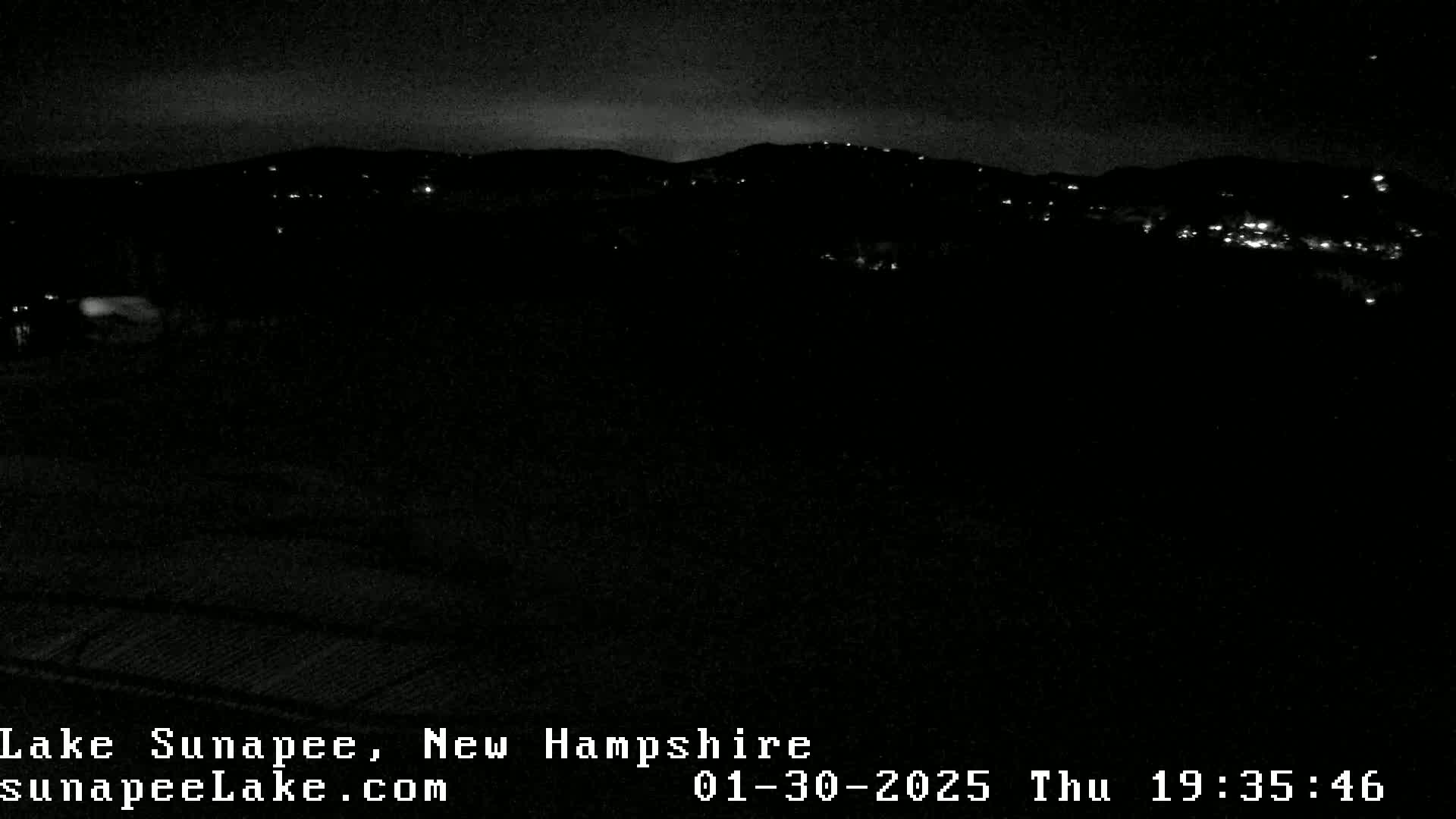 A nighttime long shot of dimly lit hills and a dark foreground under a clear sky.