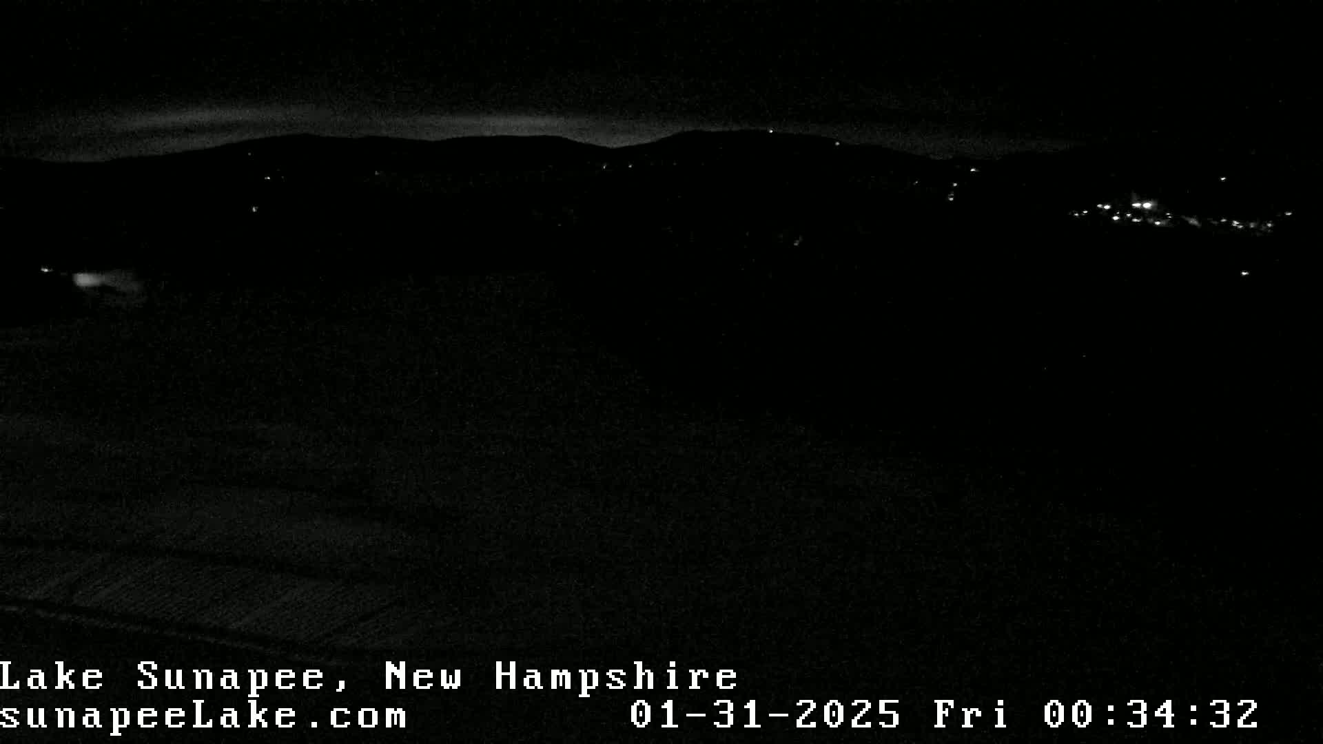 A nighttime, low-light view of a dark landscape with a few distant lights visible in the background.