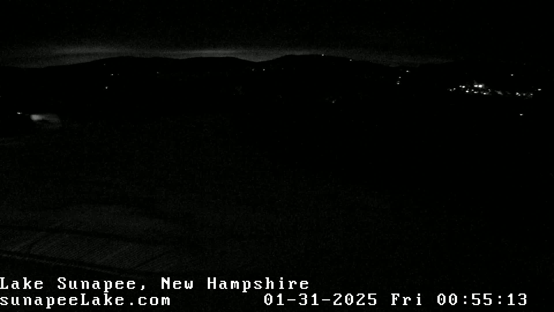 A nighttime, low-light view of a dark landscape with a few distant lights and a dark sky.