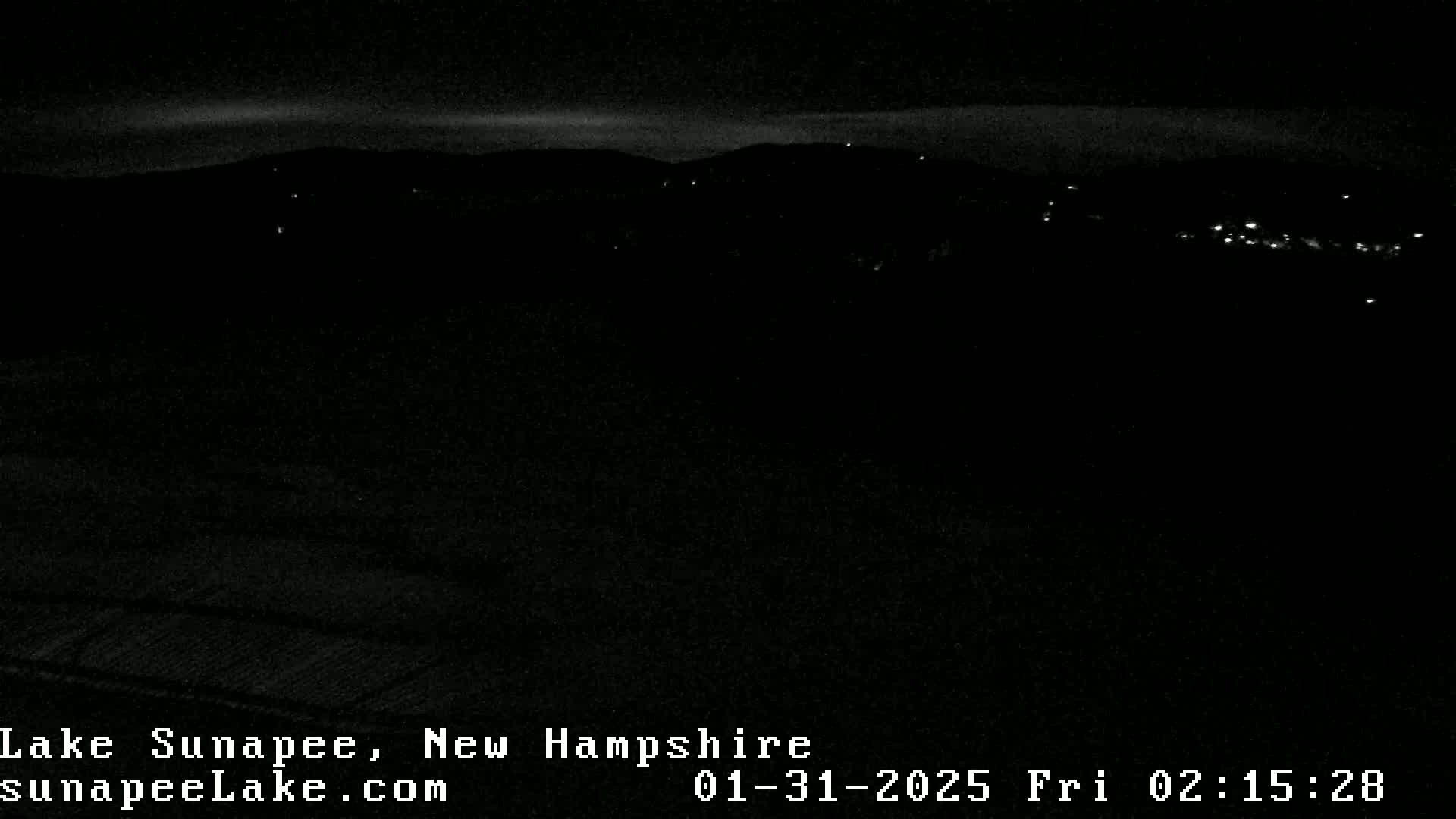 A nighttime long shot shows a dark landscape with a few faint lights in the distance under a mostly clear sky.