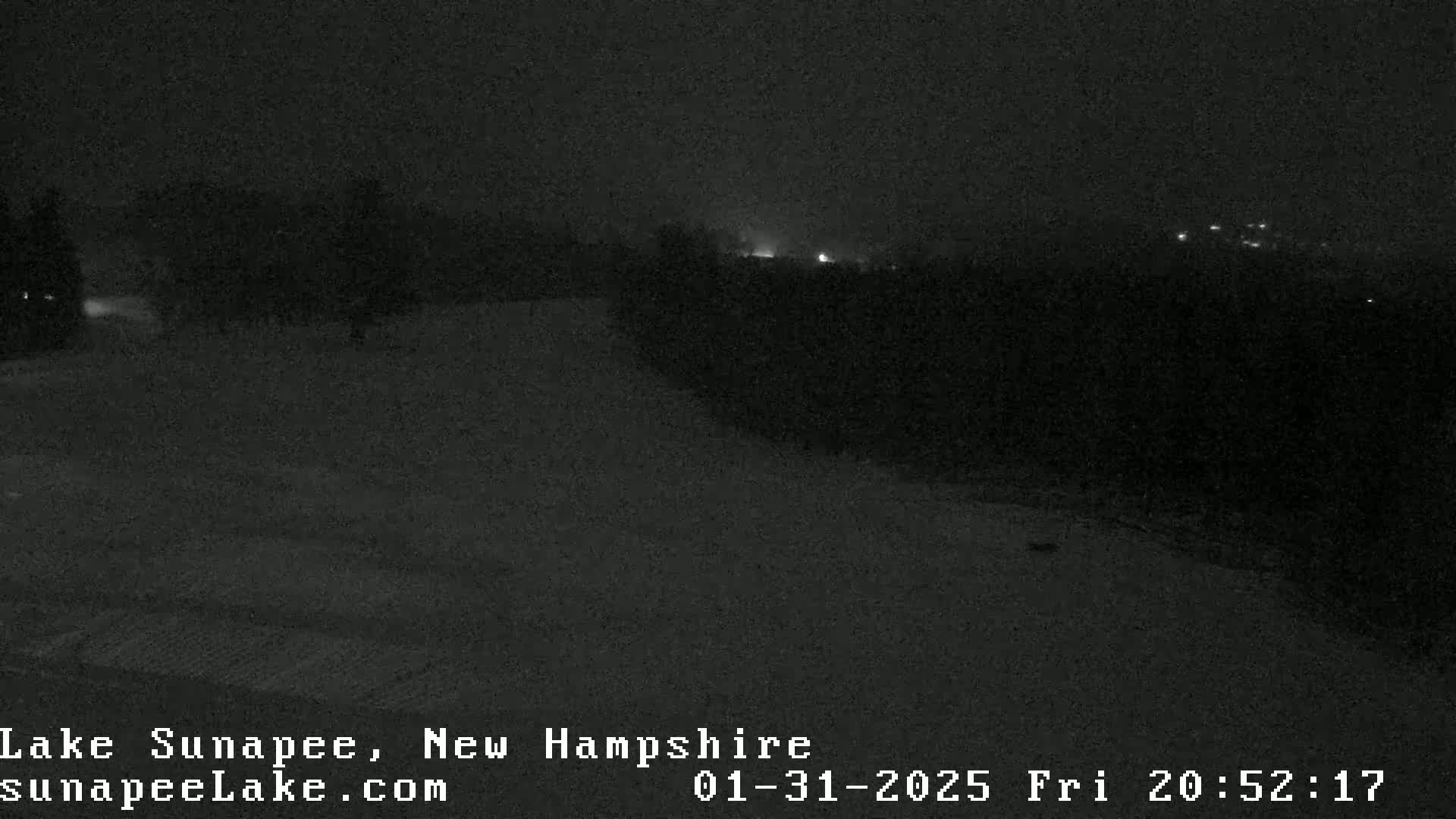 A nighttime, low-light view of a snow-covered landscape with a few distant lights visible in the background.