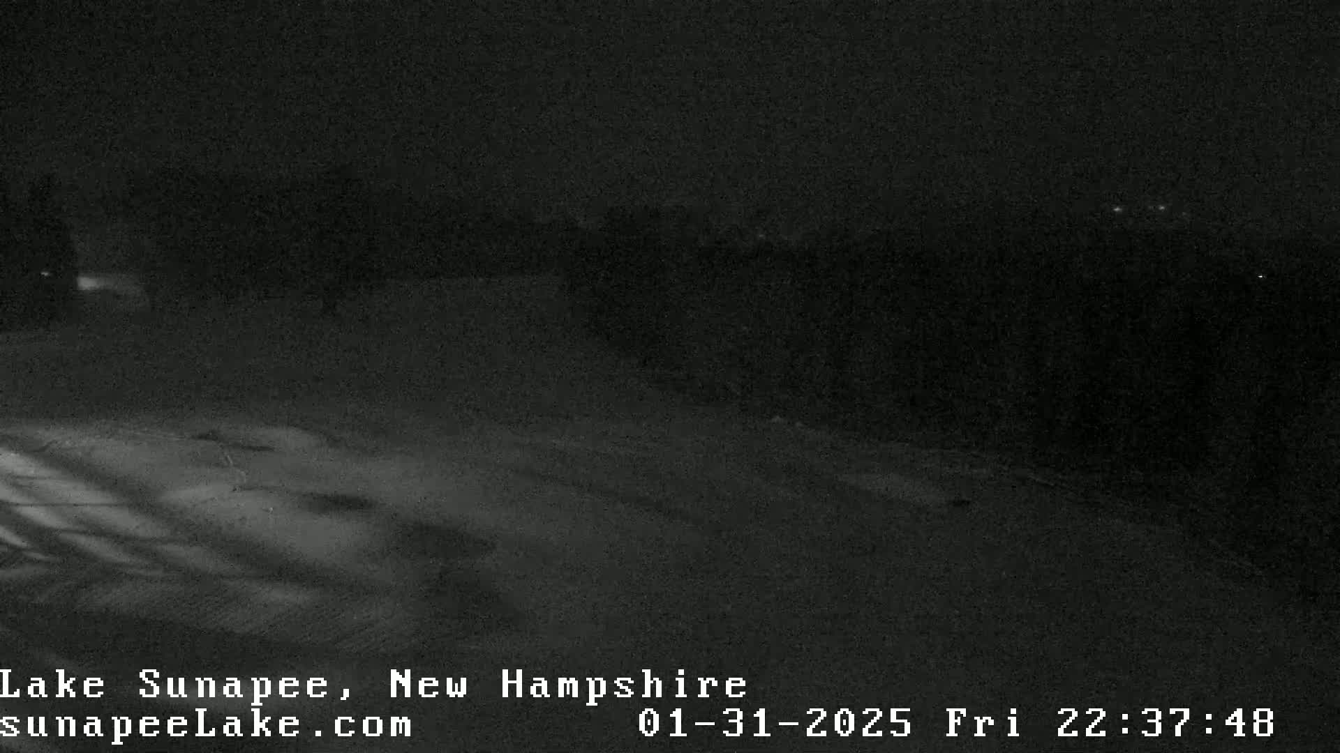A nighttime, low-light view of a snow-covered area with some distant lights visible.