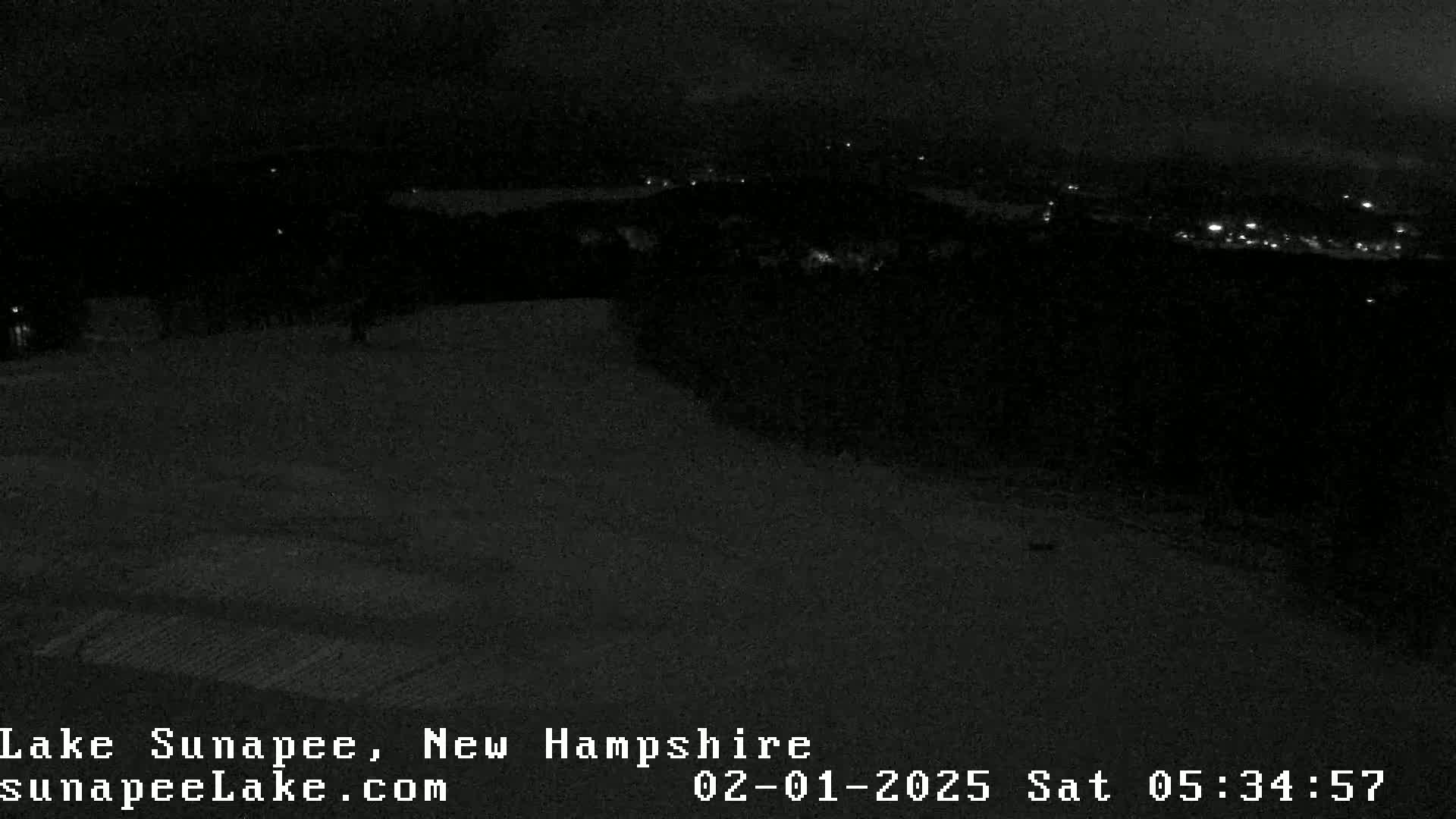 A nighttime, low-light view of a snow-covered landscape with distant lights in the background.