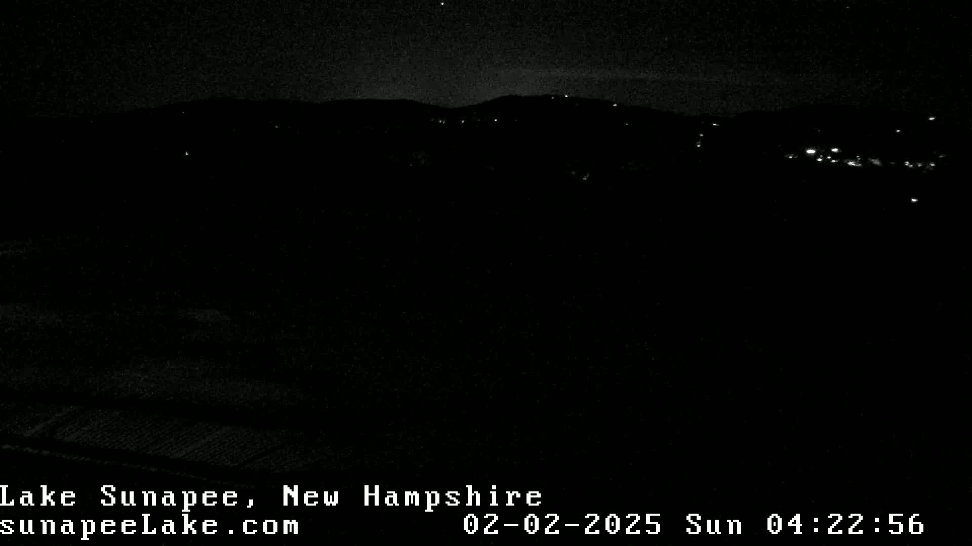 A nighttime, low-light view of a dark landscape with a few distant lights visible.