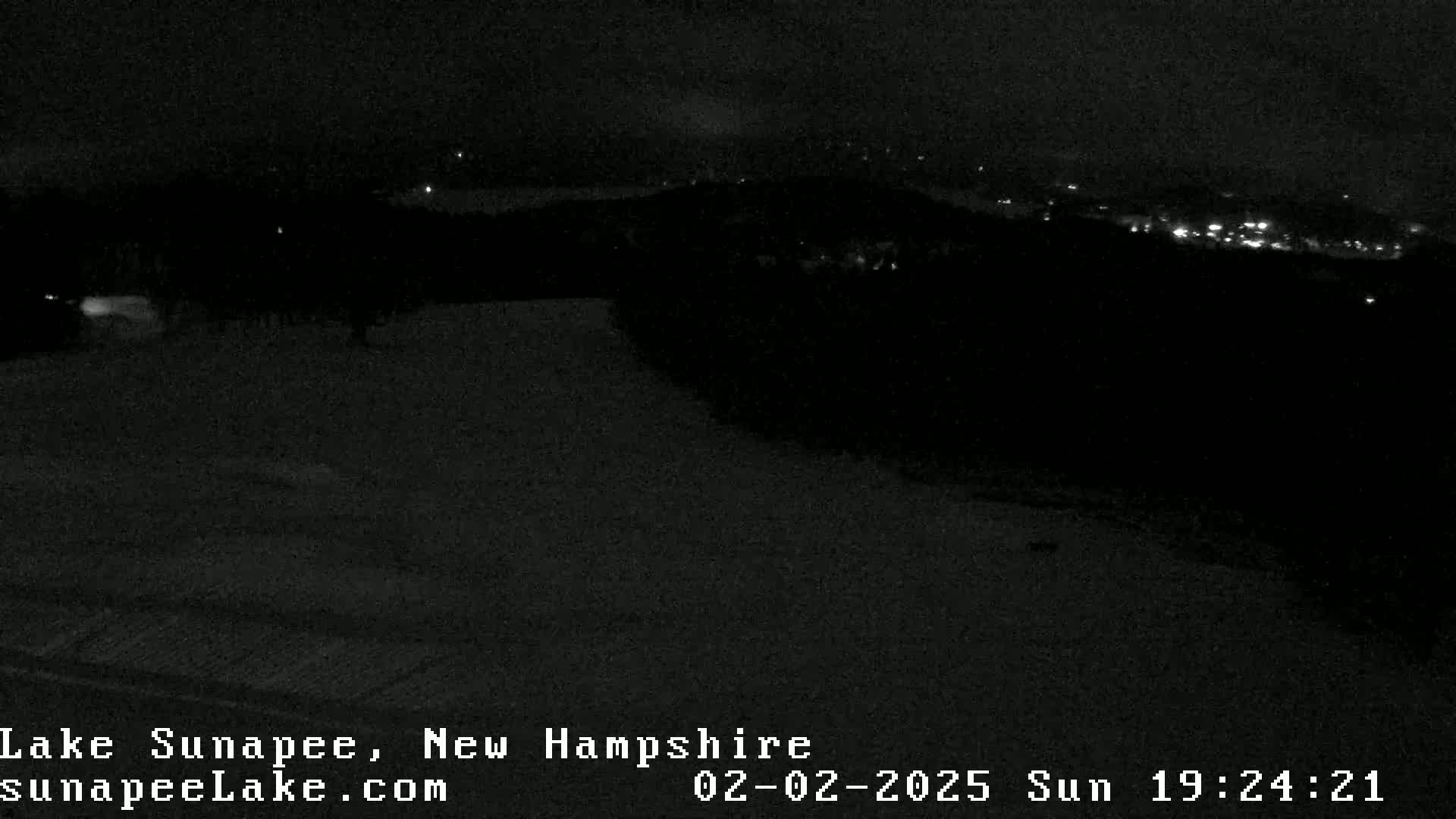 A dark, snowy landscape is visible at night, with faint lights from a distant town or city in the background.