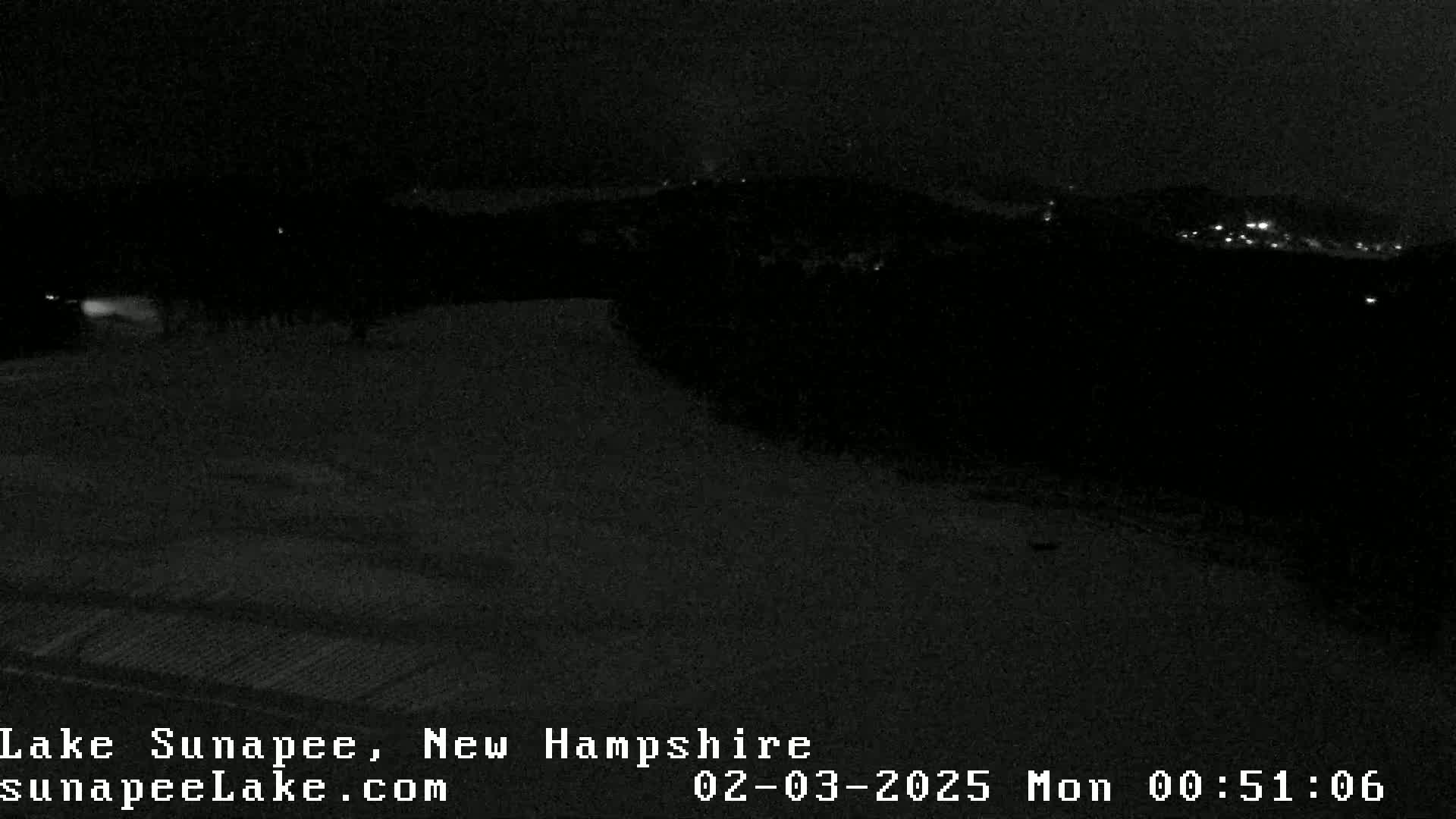A nighttime, low-light view shows a dark landscape with a few distant lights visible in the background.