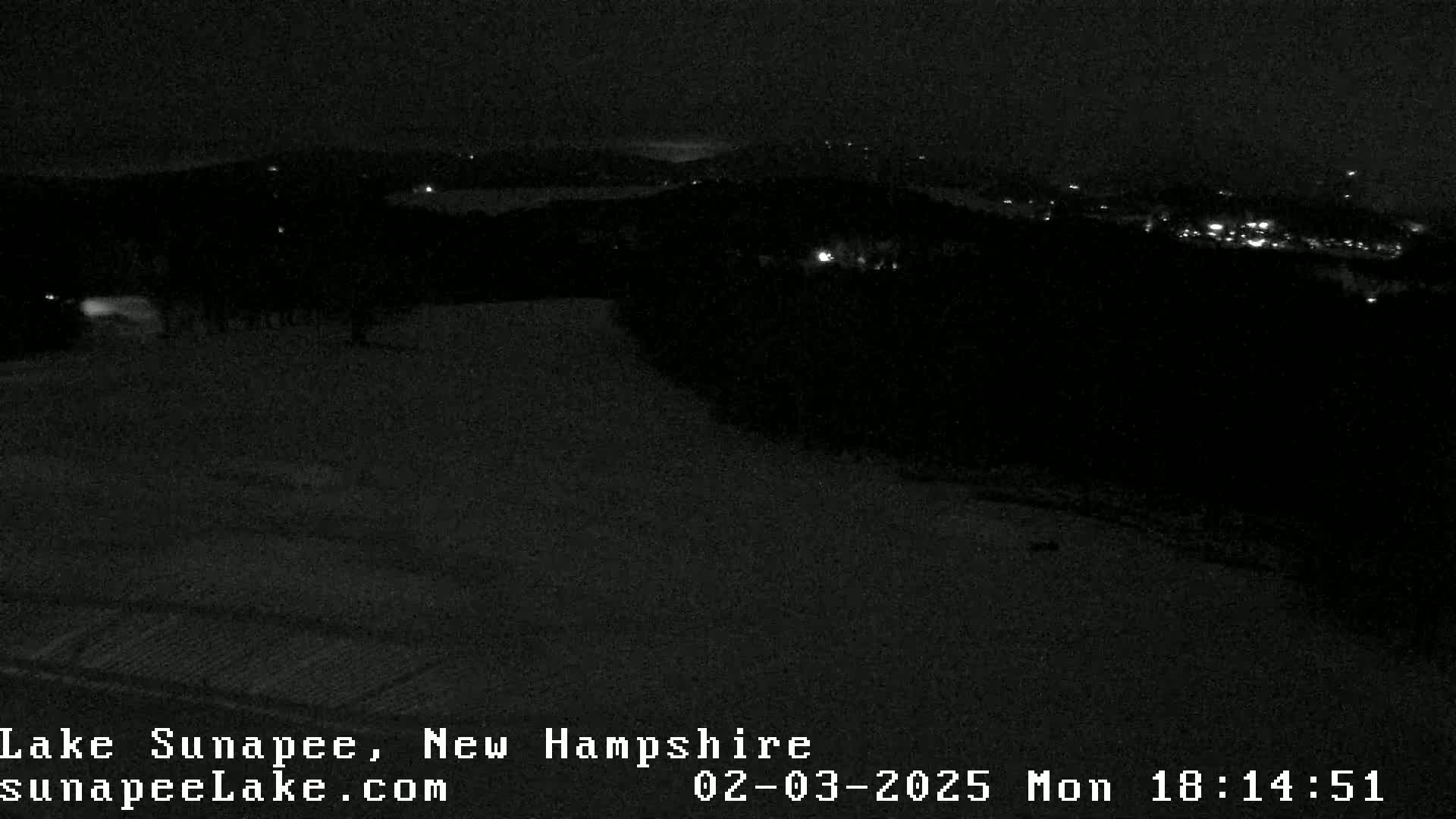 A nighttime, snow-covered landscape is visible, with a few distant lights illuminating a dark, hilly area.