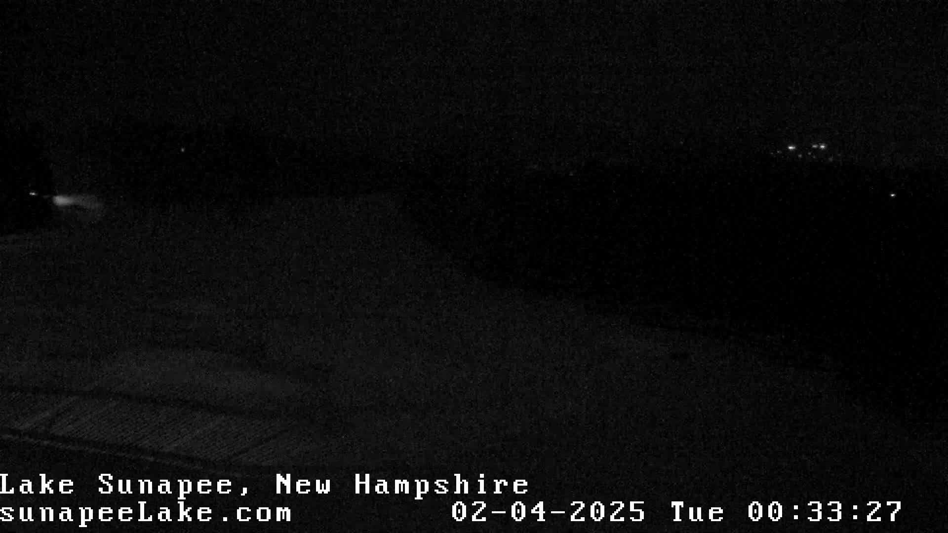 A nighttime, dark view of a landscape with faint lights visible in the distance.