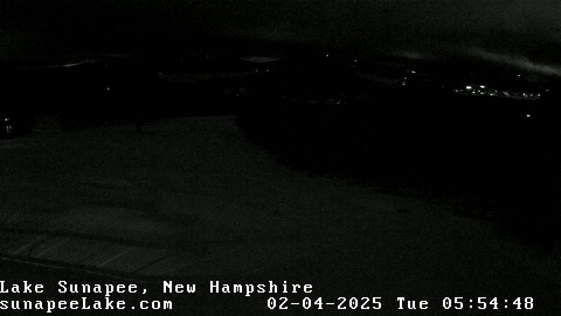 A dark, nighttime view of a snow-covered landscape with a few distant lights visible.